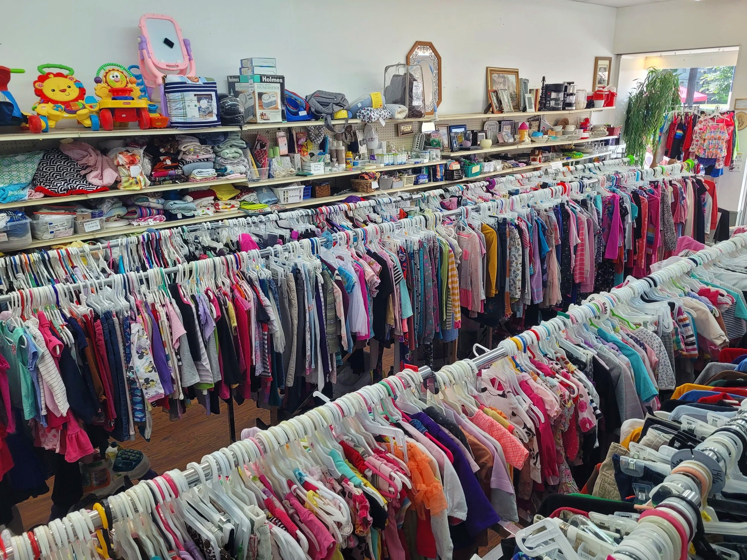 Right to Life of Shelby County thrift store, Sidney Ohio. Features clothing racks filled with children's clothes, shelves with toys, books, and household items, and a large window letting in natural light.