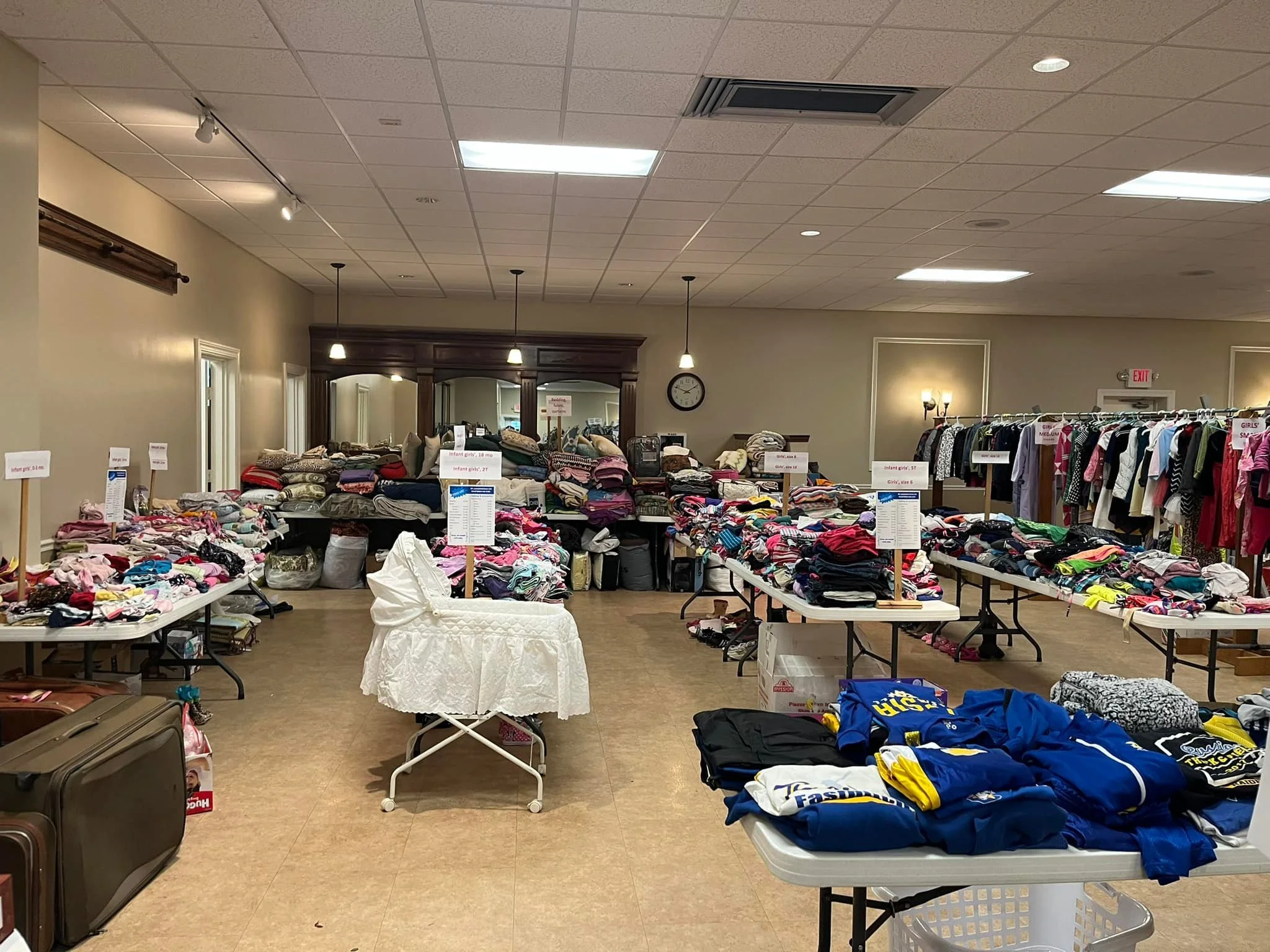 Tables displaying various items like folded baby clothes, children's clothes, and apparel in a thrift store or donation center setting.