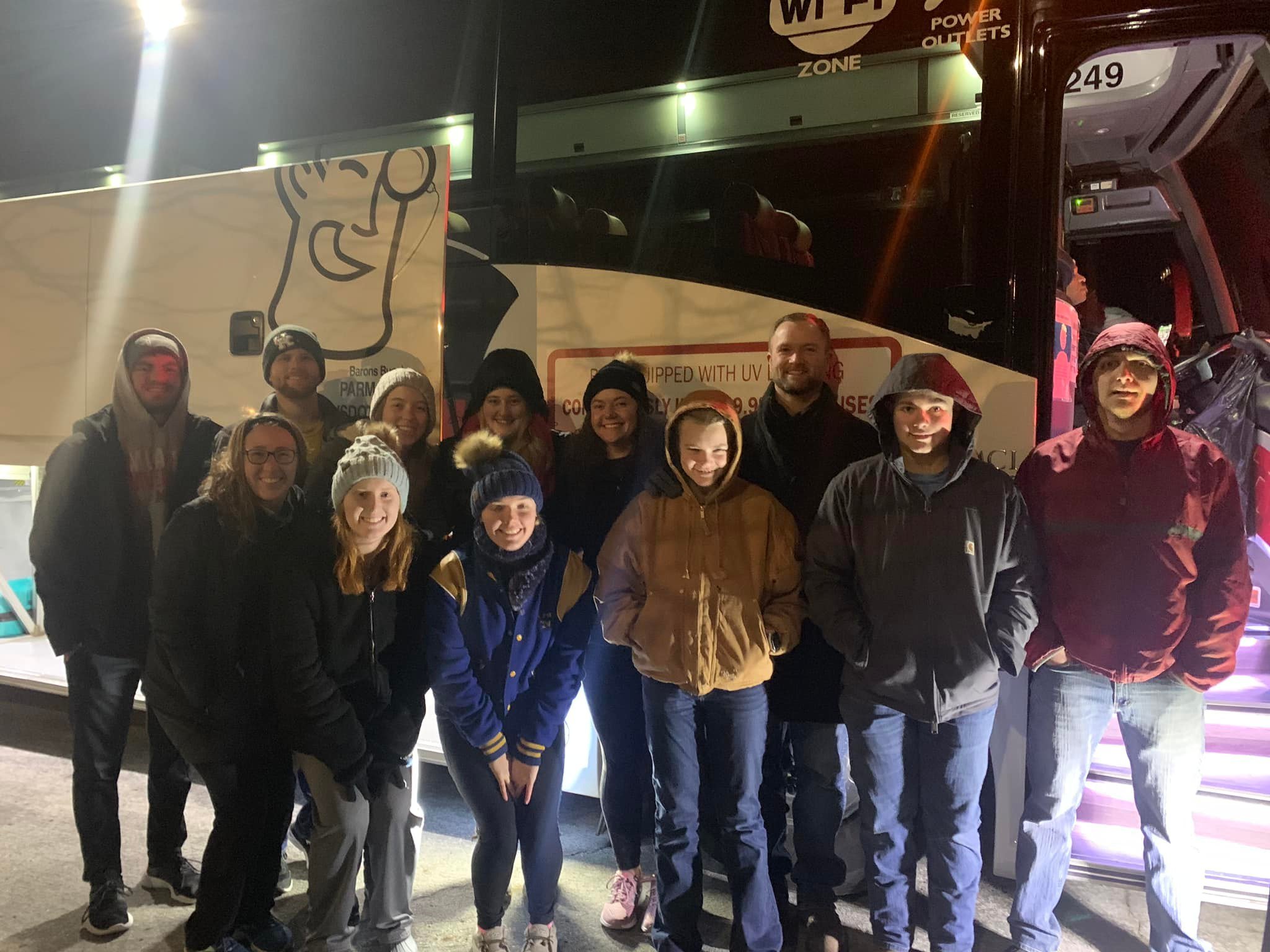 Group of people standing in front of a March for Life bus at night, some smiling and wearing jackets and winter hats.