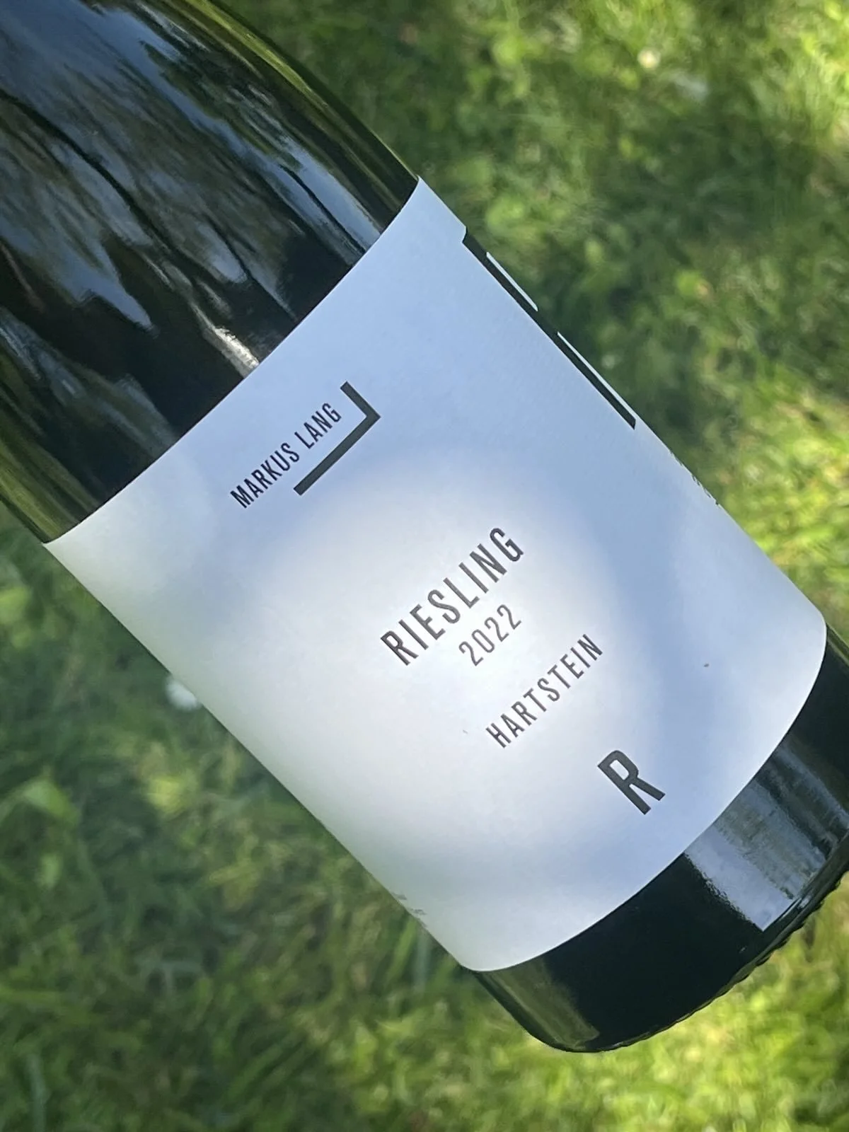 Eine Flasche Wein mit kleinem, weißem Etikett auf grünem Gras.