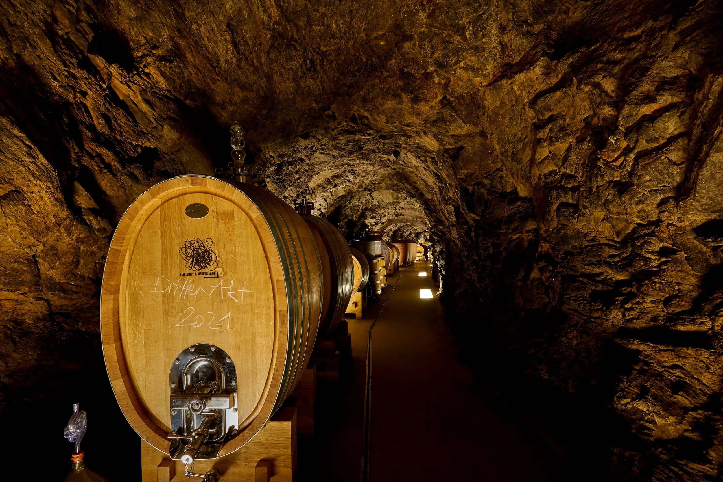 Weinlager in einem Weinkeller mit Holzfässern in einer Felsenkaverne, beleuchtet mit warmem Licht.