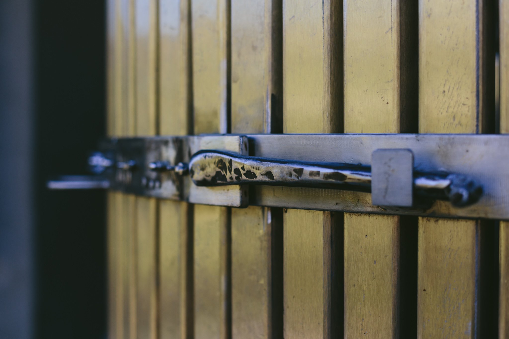 Nahaufnahme eines gelb gestrichenen Holz- und Metalschiebetores mit einem schwarzen Metallgriff.