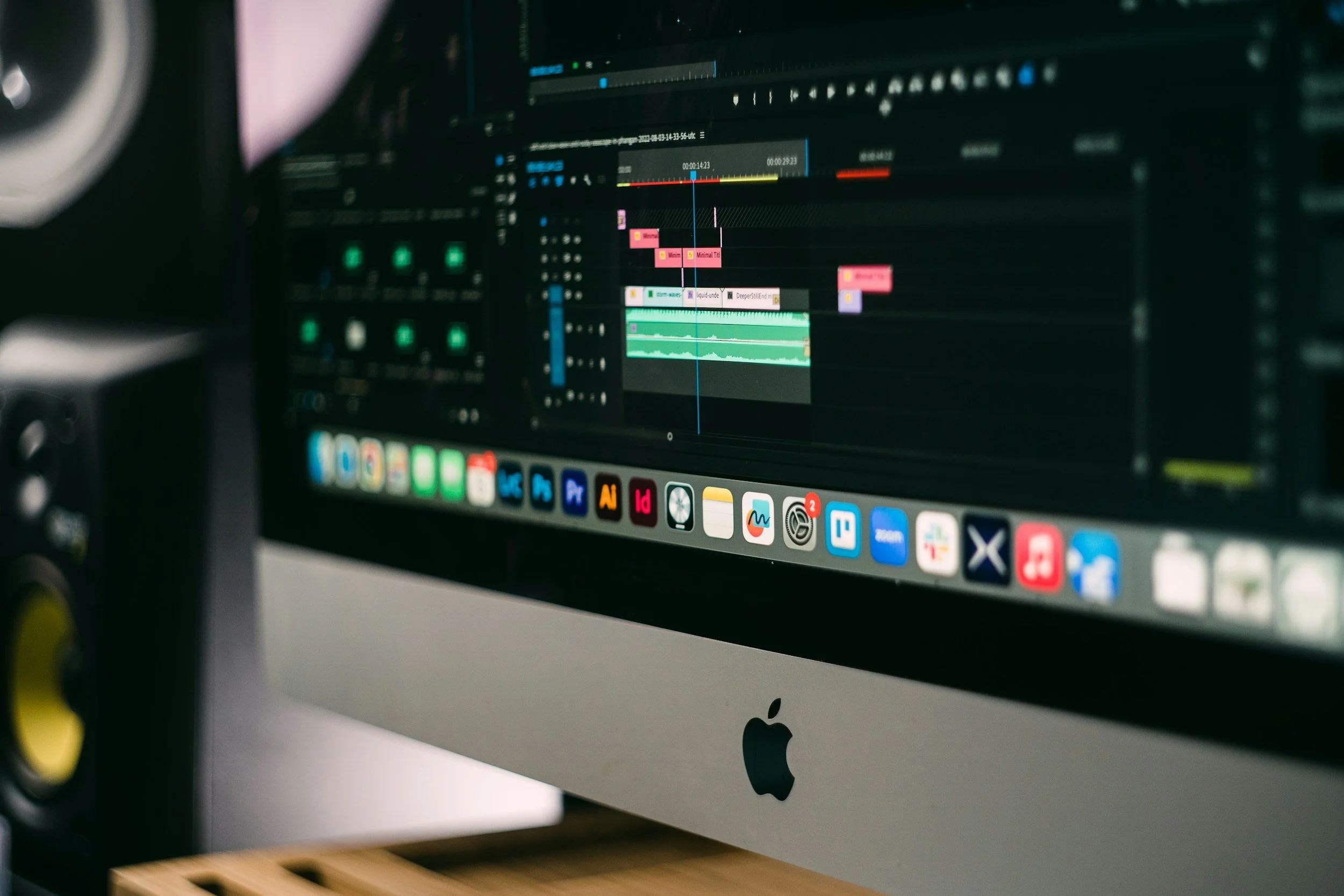Close-up of a computer monitor showing a video editing software interface with colorful audio and video tracks, icons on the dock below, and a dark background.