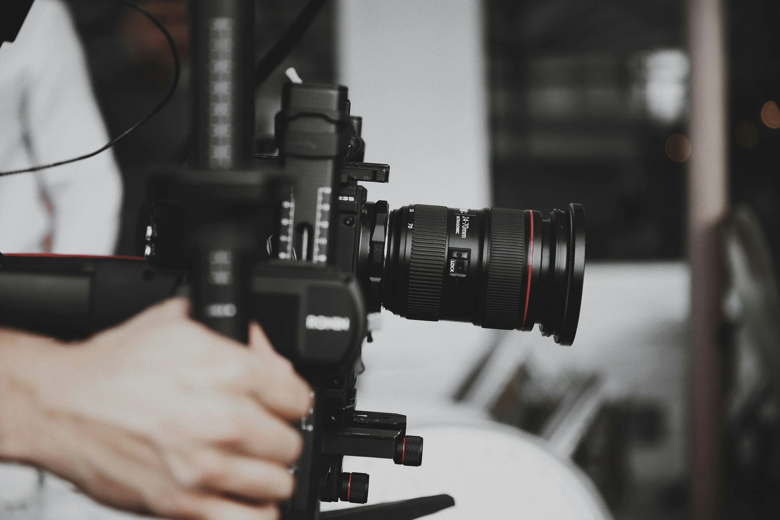 A person operating a professional video camera with a large lens, mounted on a tripod.