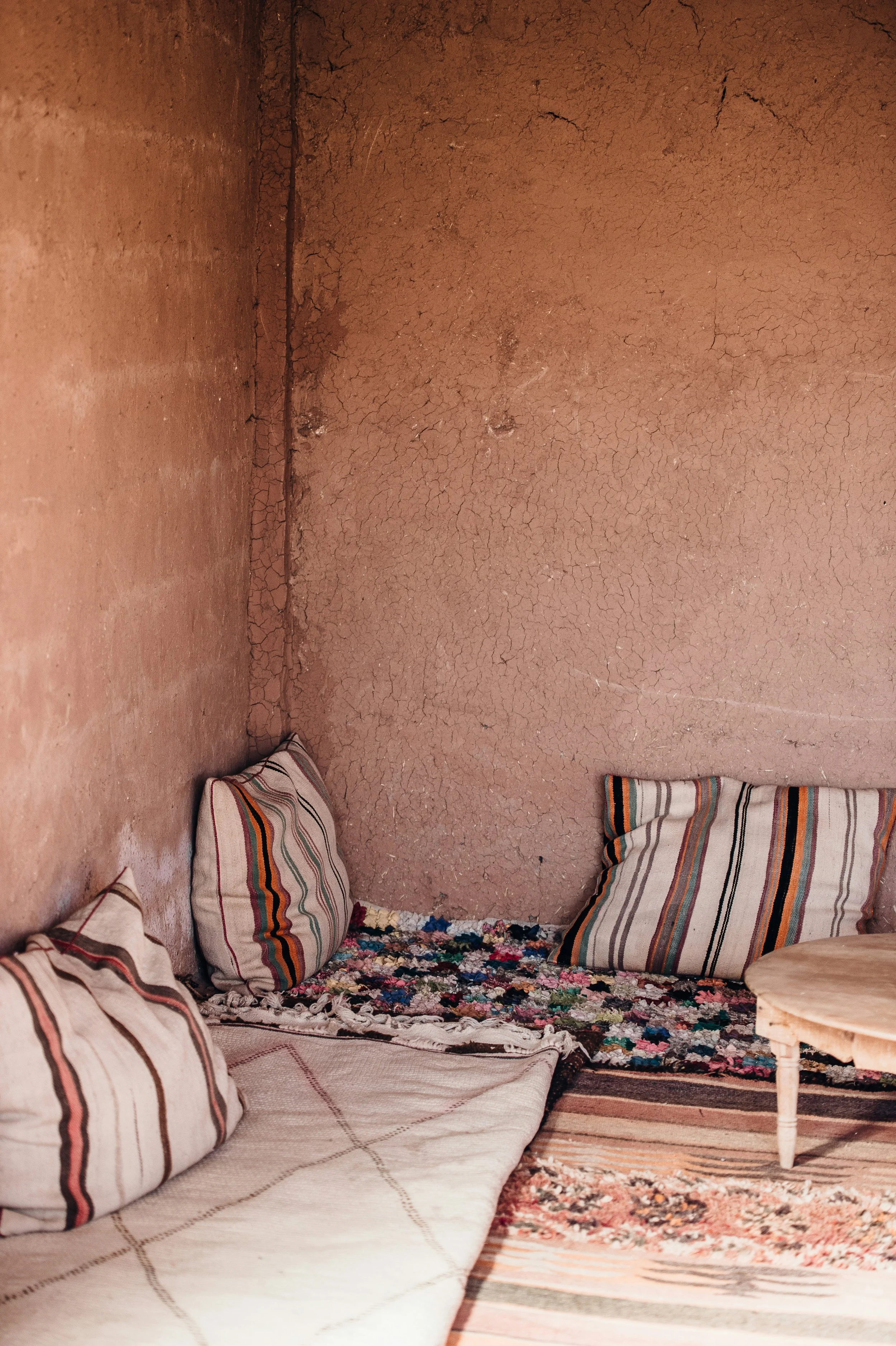 A cozy floor seating arrangement with striped cushions and floral rugs in a rustic, earthen-walled room.