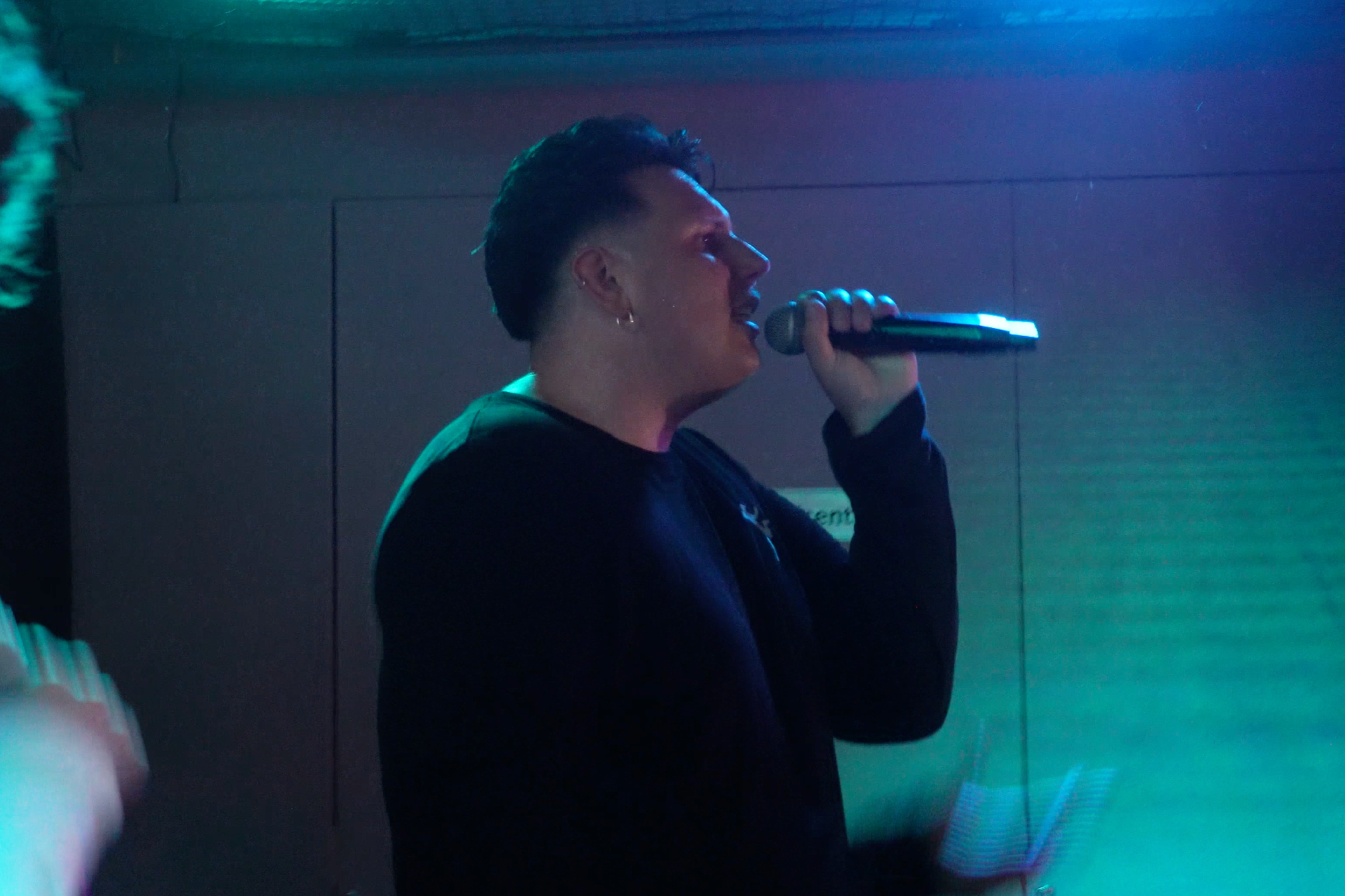 Person som sjunger eller talar in i en mikrofon i en mörk, färgad belysning.