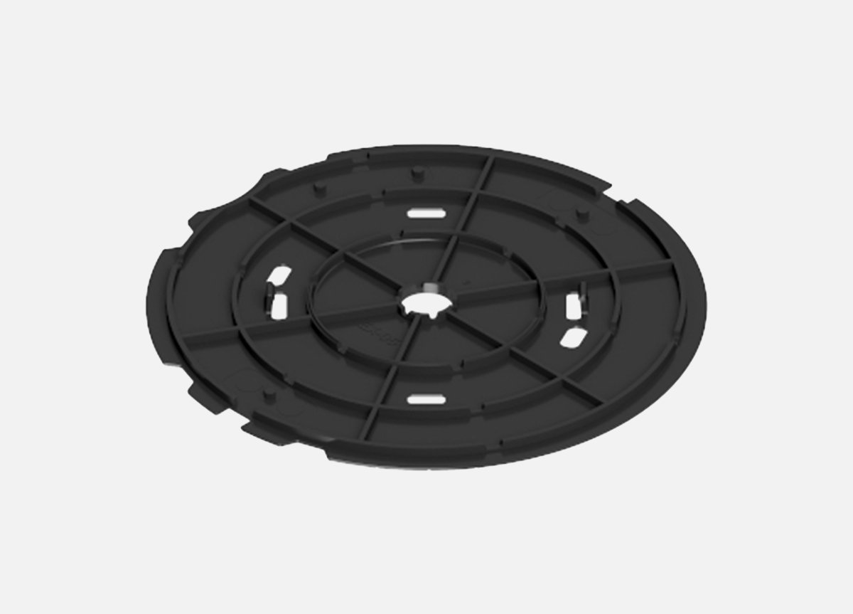 A black circular plastic component with a central hole and multiple smaller holes and slots, possibly a mounting or base plate for a device or fixture.