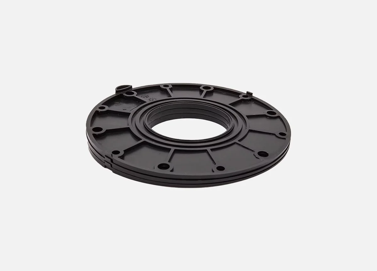 Black circular mechanical part with multiple holes around the edge, on a plain light gray background.