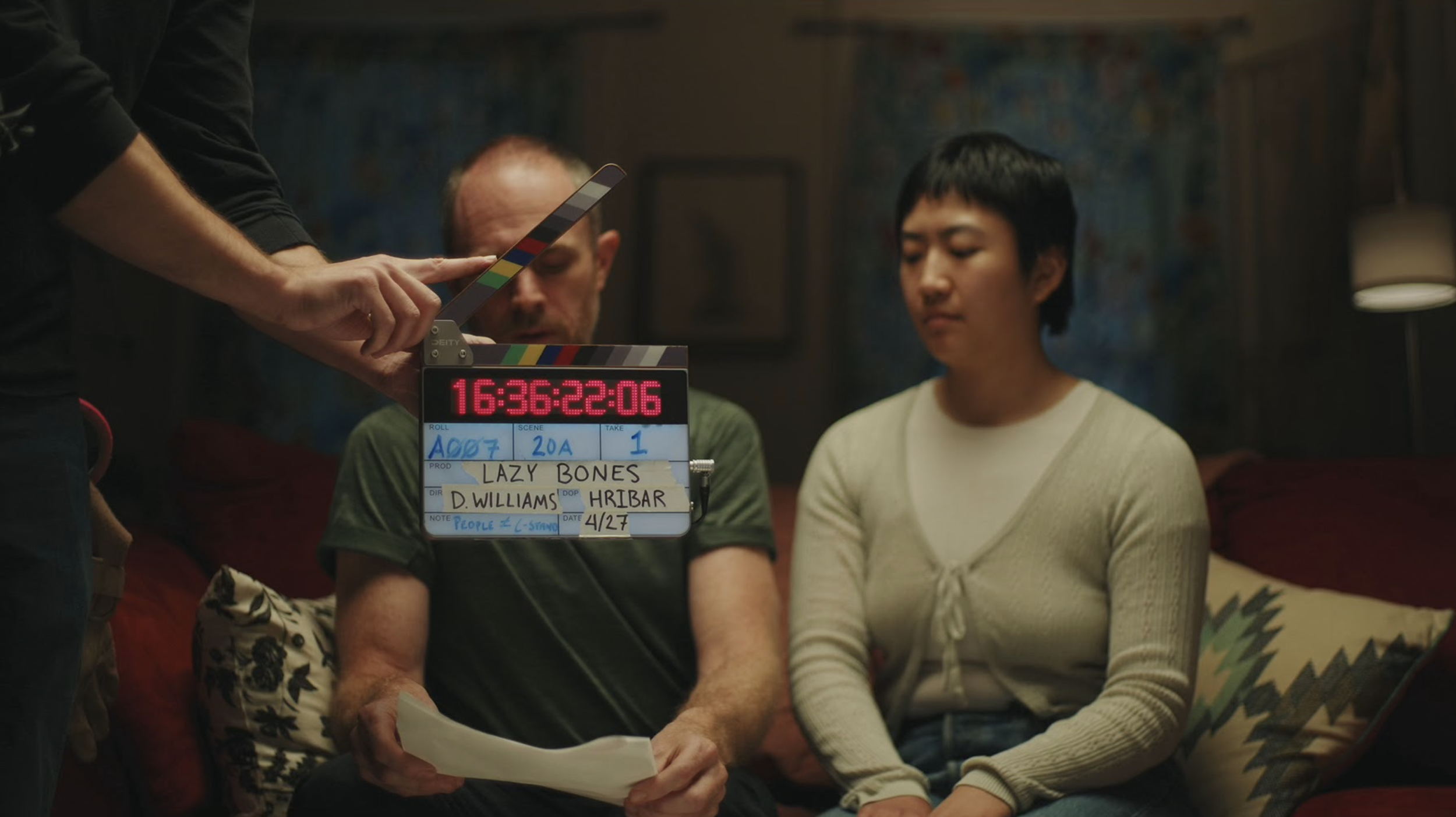 Scene being filmed with a clapperboard, two people sitting, one holding a script.