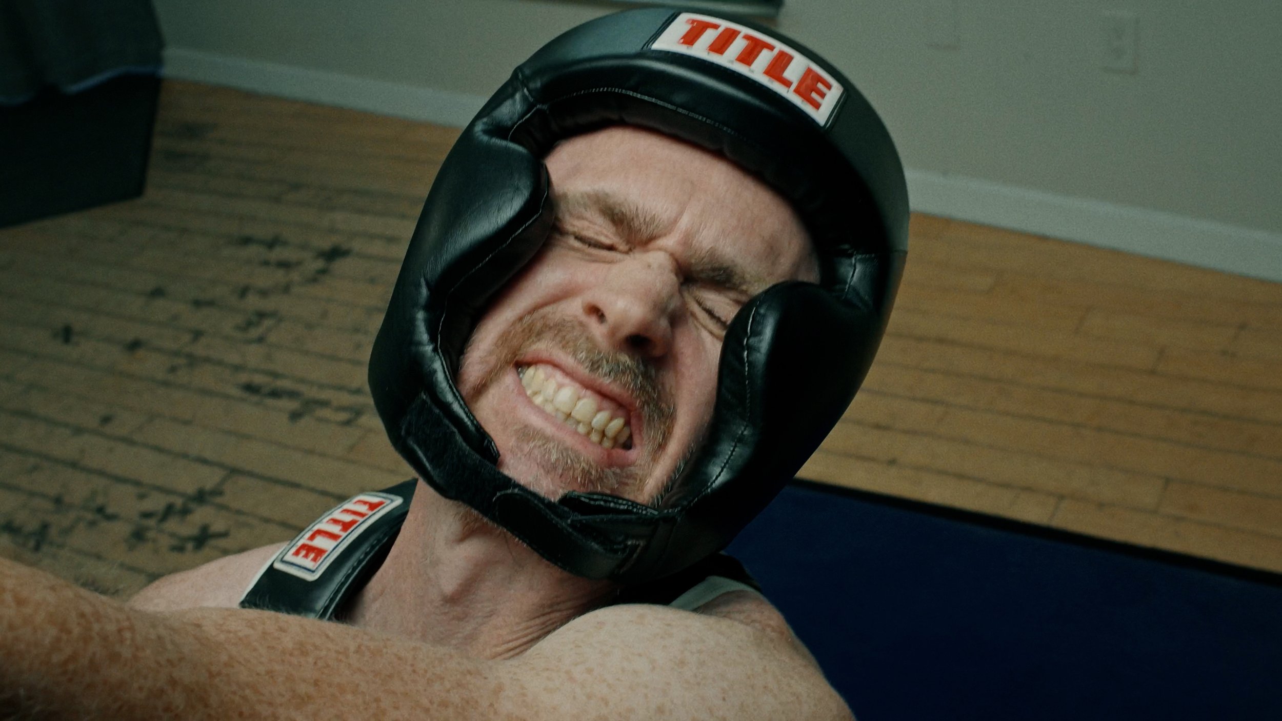 A person wearing a black boxing headguard grimacing during a match, with visible effort on their face.