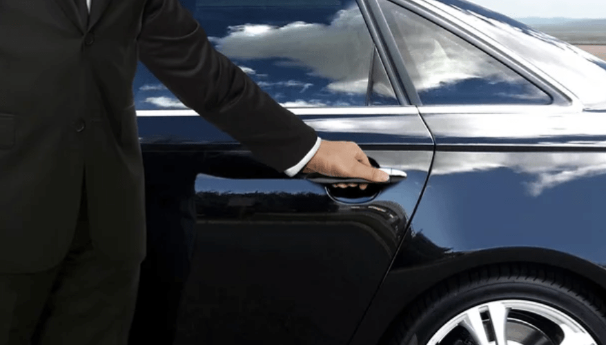 Person in a suit opening the door of a black luxury car