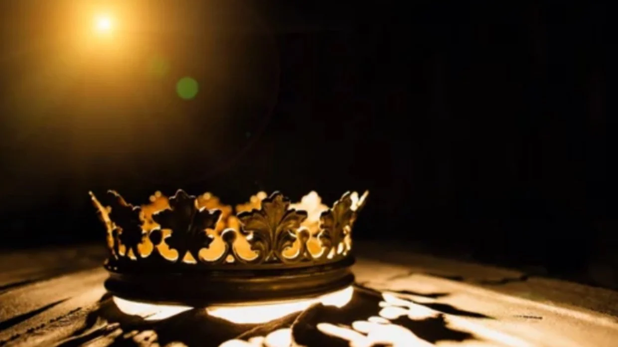 Ornate gold crown with intricate patterns under a warm light on a dark background.