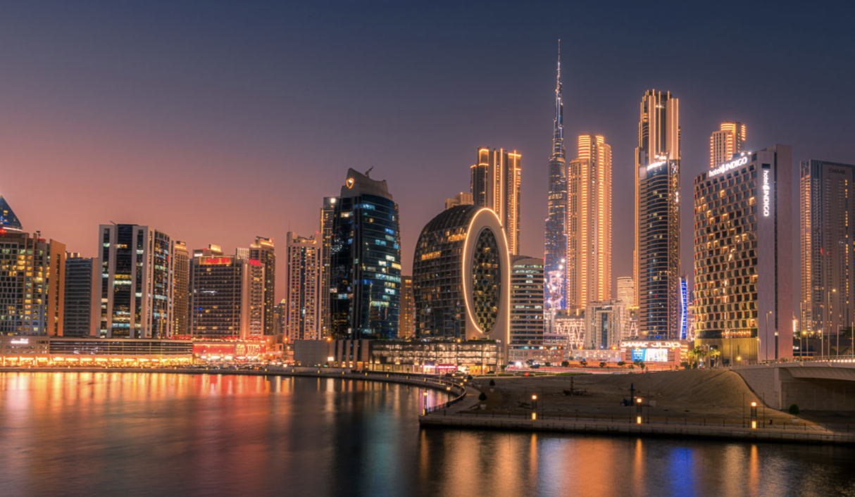 Night view of Dubai skyline with illuminated skyscrapers reflecting in the water.