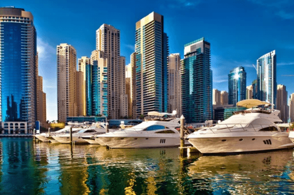 Luxury yachts docked in a marina with modern skyscrapers in the background.