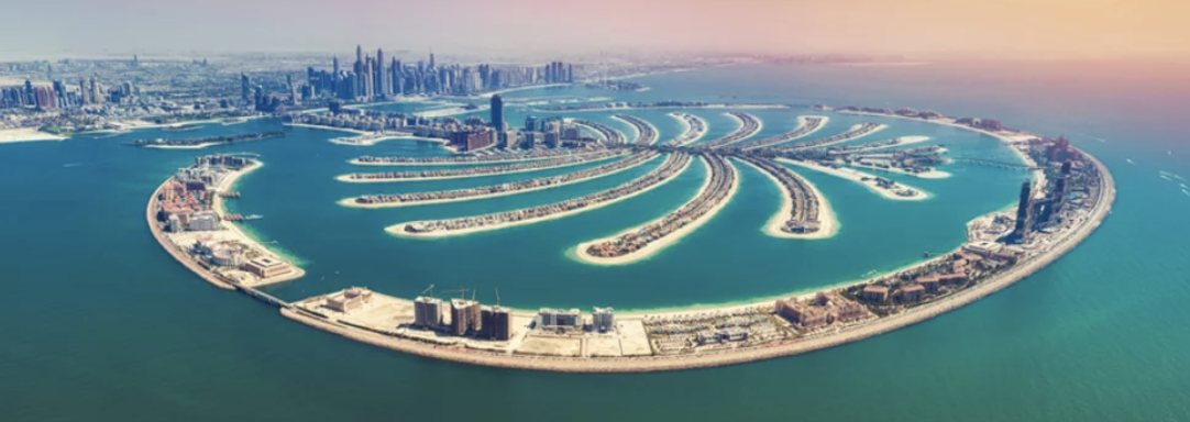 Aerial view of Palm Jumeirah in Dubai, featuring crescent and frond shapes surrounded by ocean, with city skyline in the background.