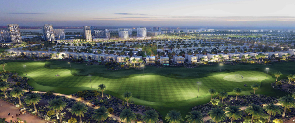 Aerial view of a modern residential community with a golf course and palm trees at dusk. Several houses are visible along with taller buildings in the background, illuminated by lights. The sky appears to be transitioning from day to night.