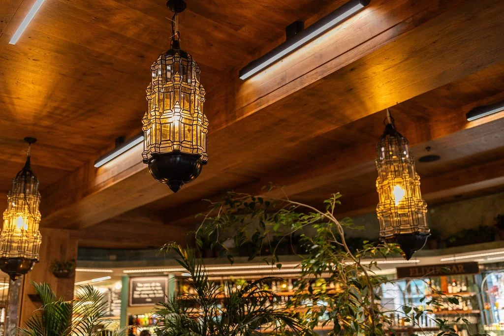 Interior of a restaurant with wooden ceiling, tropical plants, and decorative hanging lantern lights.