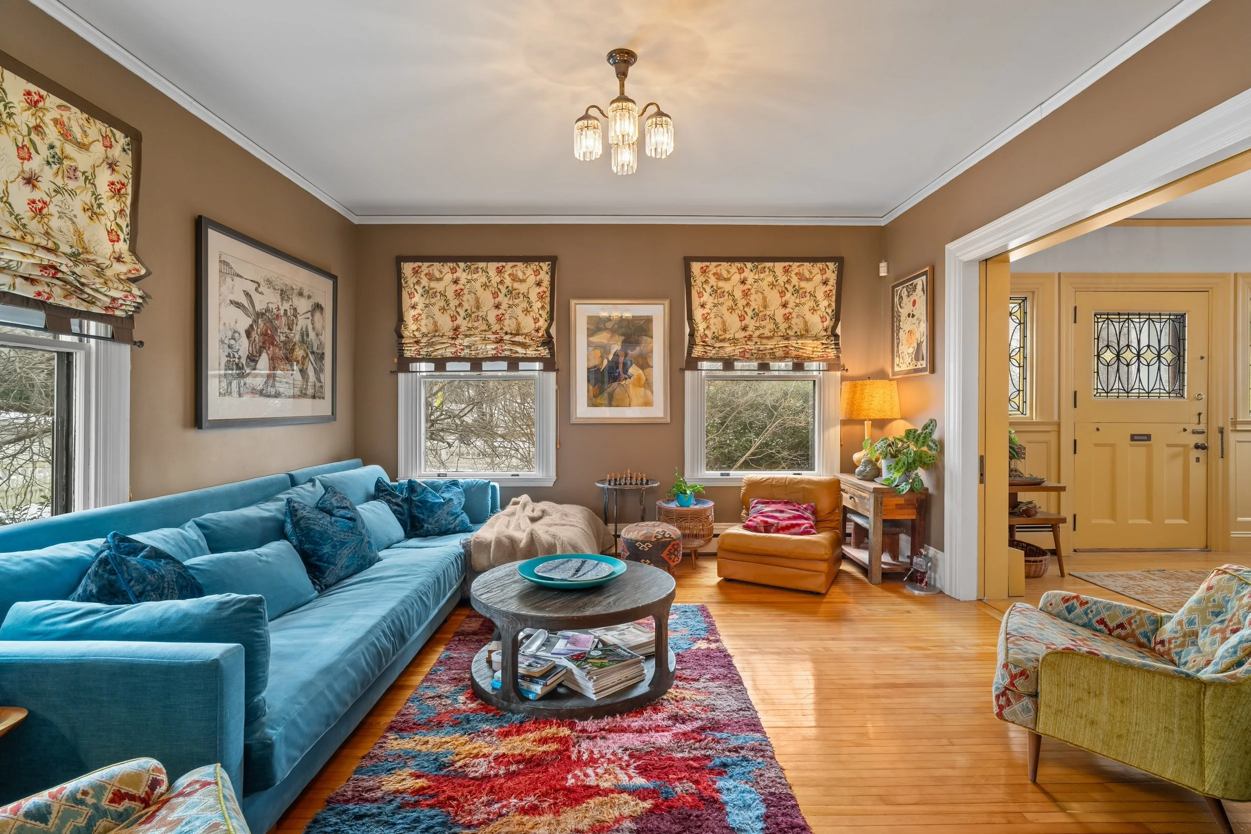 Living room with a blue sofa, colorful rug, and windows with floral Roman shades.