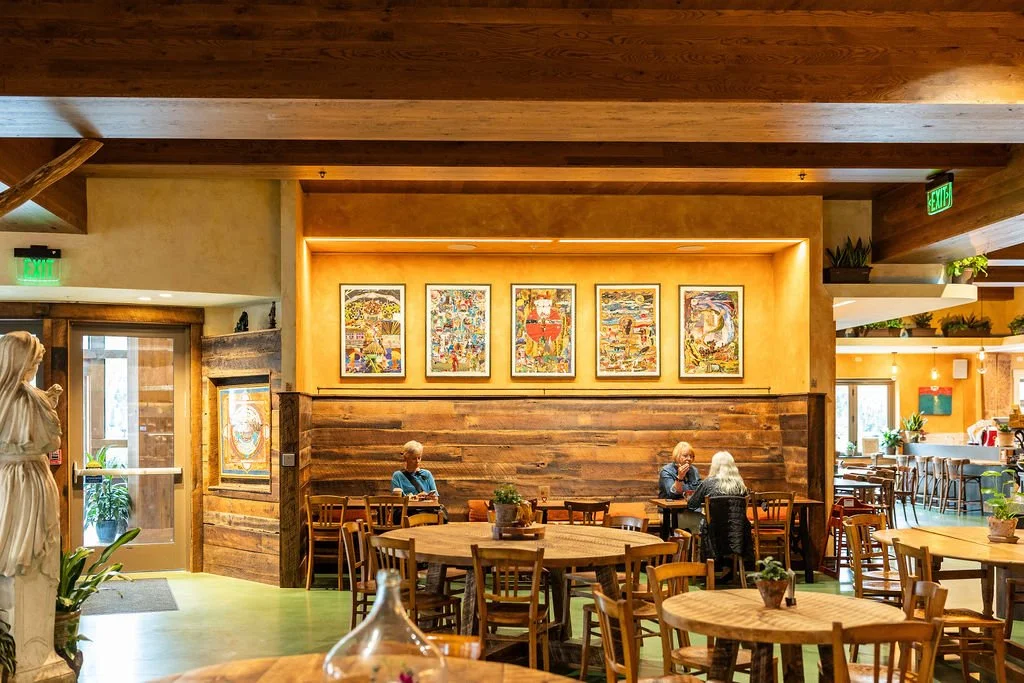 Interior of a cozy restaurant with wooden furniture, artwork on the walls, and a few elderly people dining.