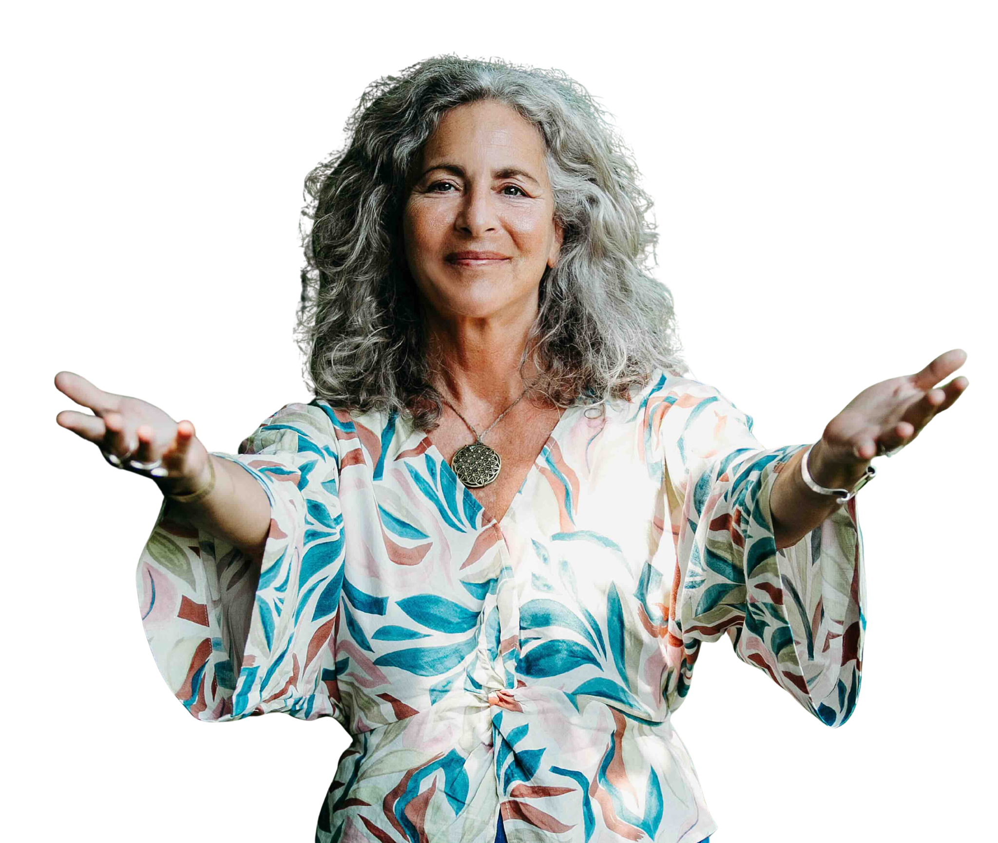 An older woman with curly gray hair stands with her arms open and a welcoming smile, wearing a colorful tropical-print blouse and a pendant necklace.