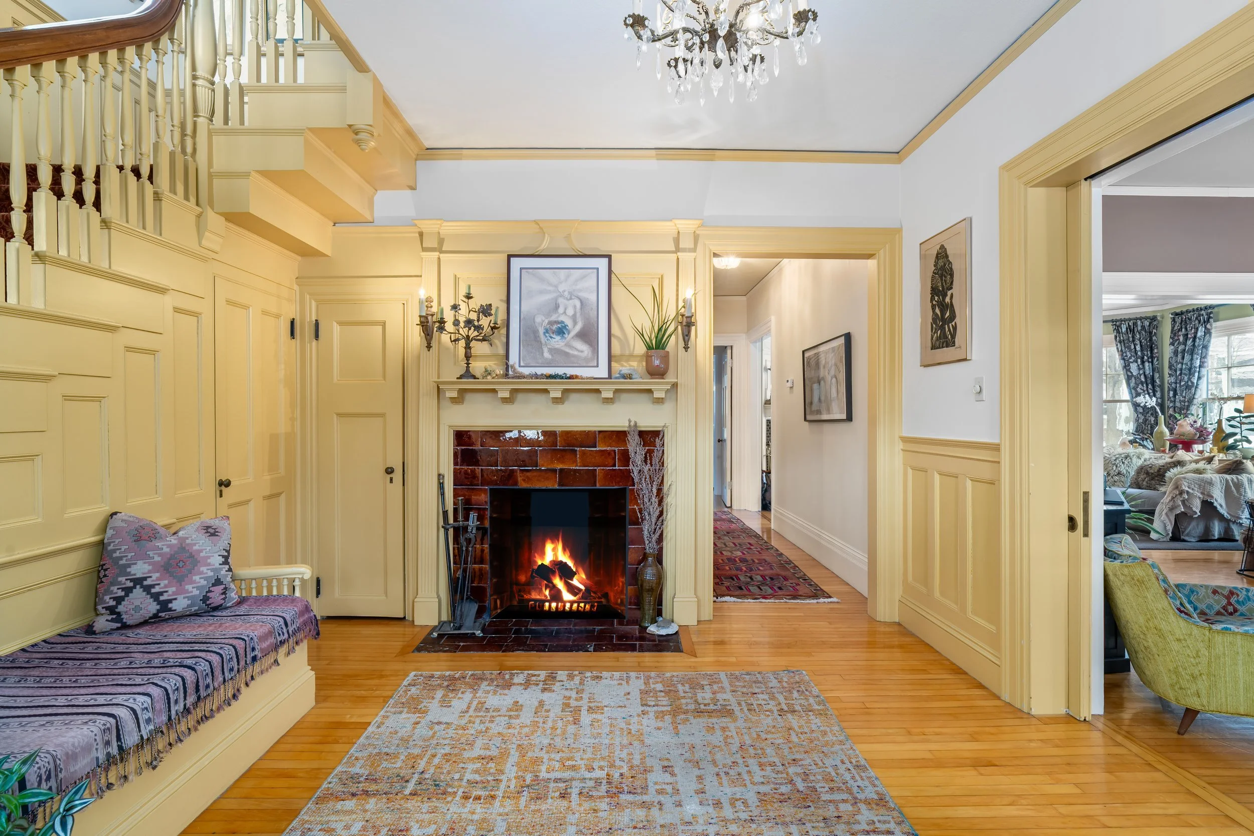 Living room with a brick fireplace, yellow paneled walls, a wooden floor, a patterned rug, and a bench with a cushion.