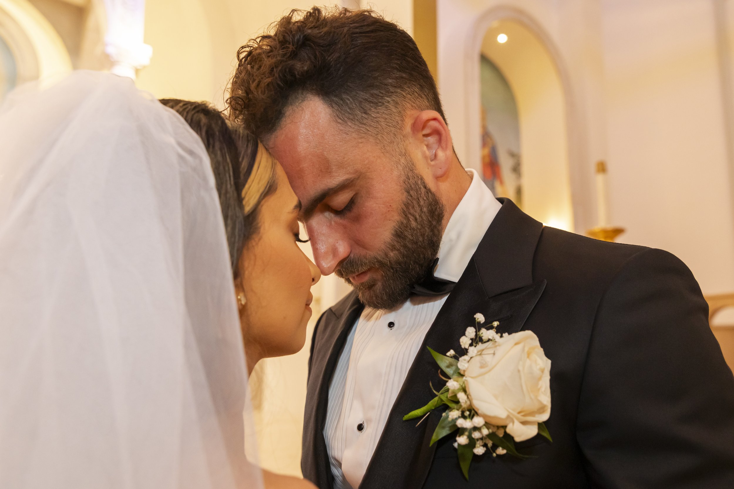 A bride and groom with foreheads touching inside a church during a wedding ceremony.
