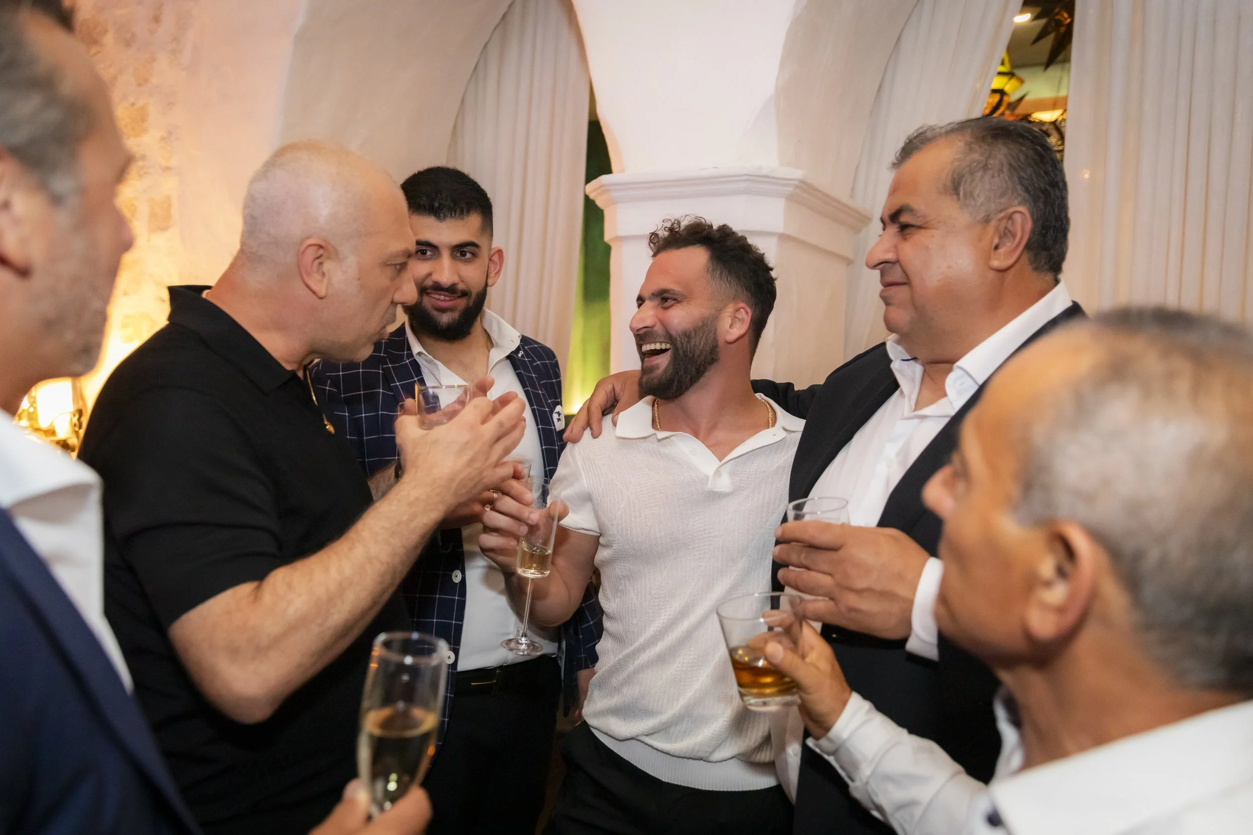 Group of men talking and laughing while holding drinks at a social gathering.