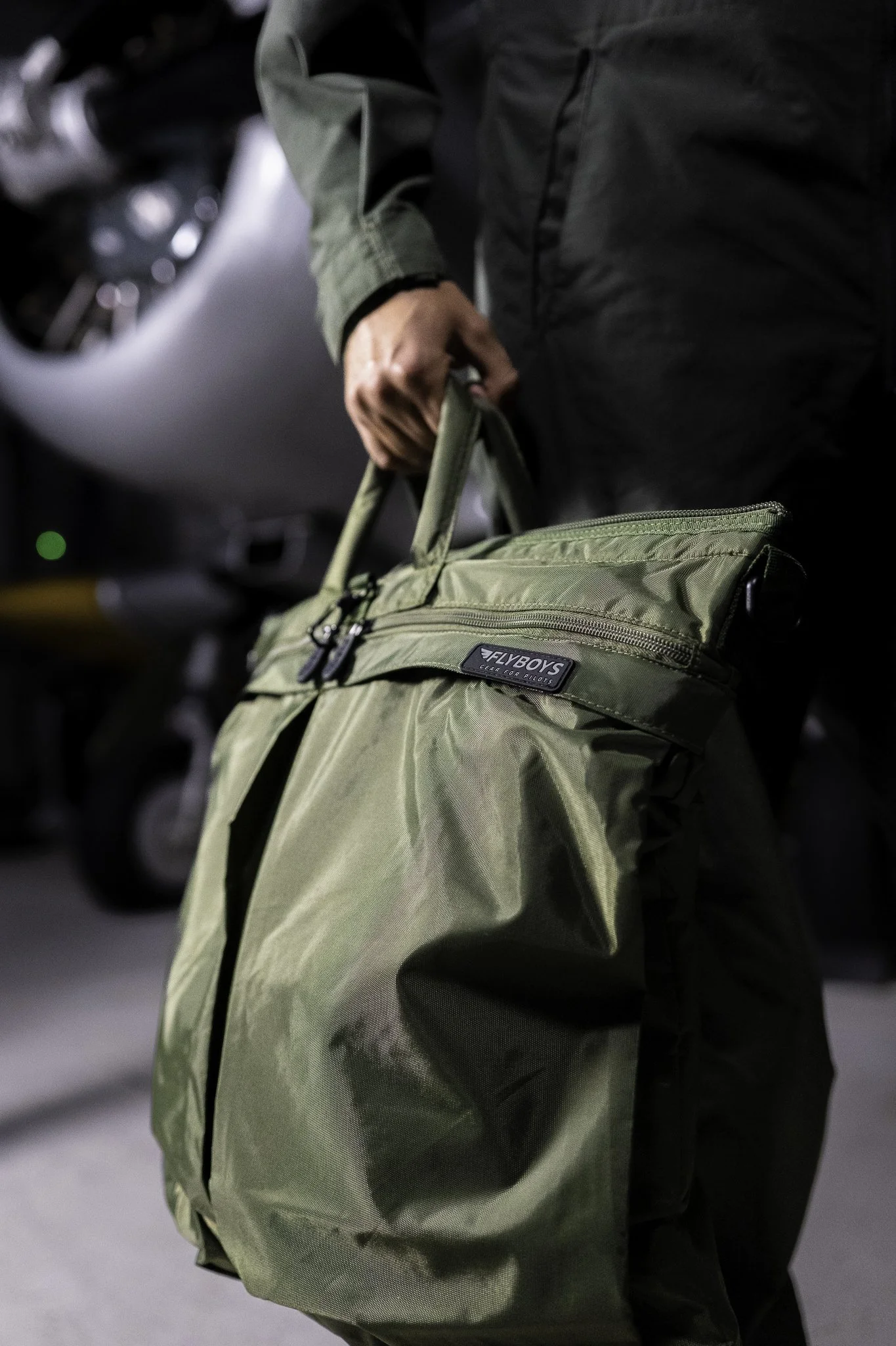 Person holding a green Flyboyz travel bag in an indoor parking garage.