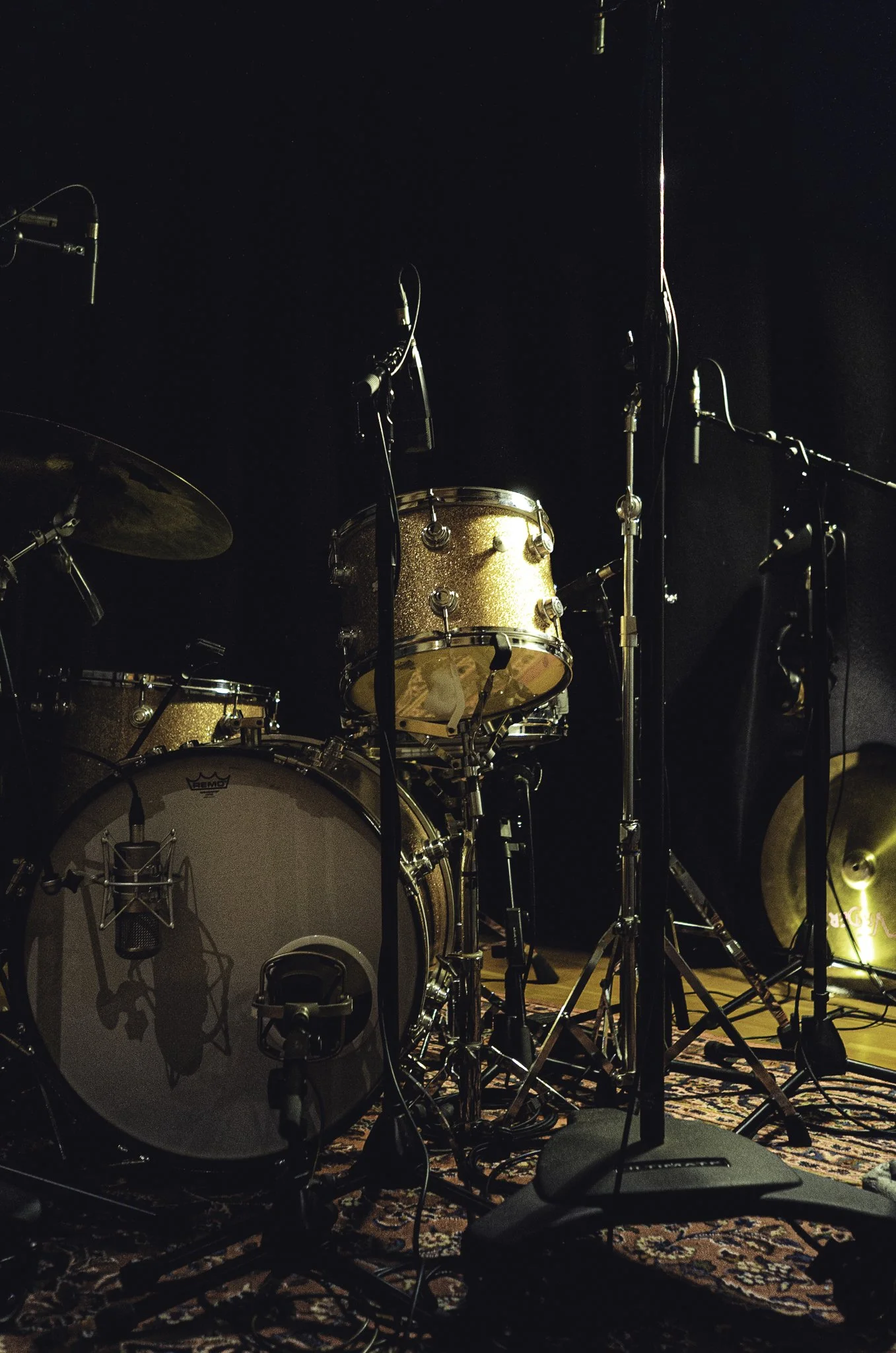 A drum set in a studio with multiple microphones on a patterned rug.