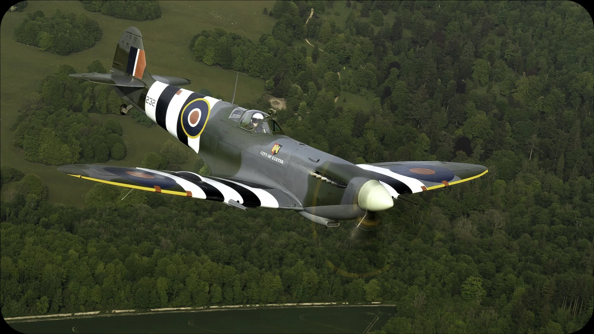 A vintage military aircraft flying over a forested area.