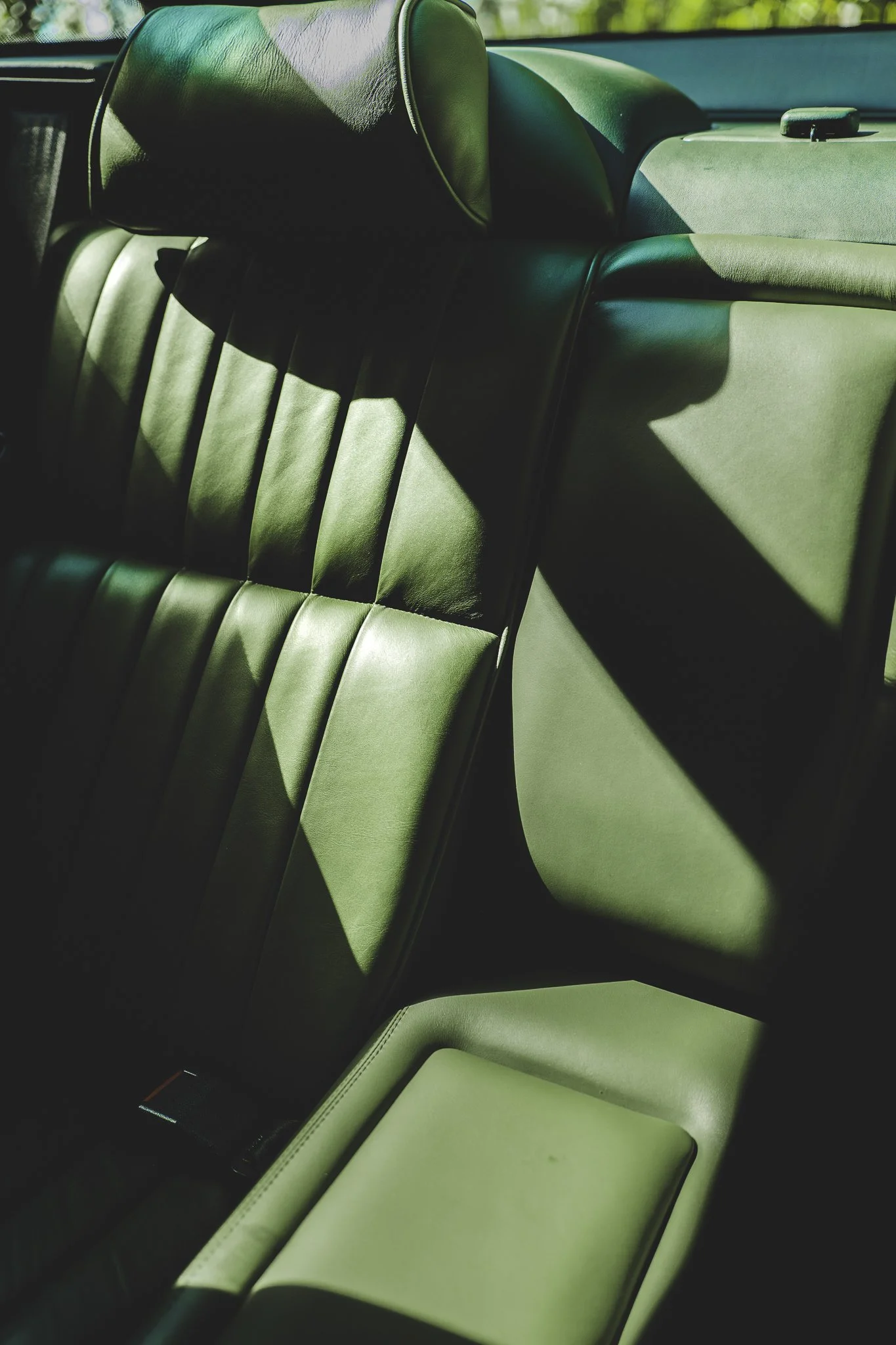 Close-up of the green leather backseat in a car with sunlight casting shadows on the seat.
