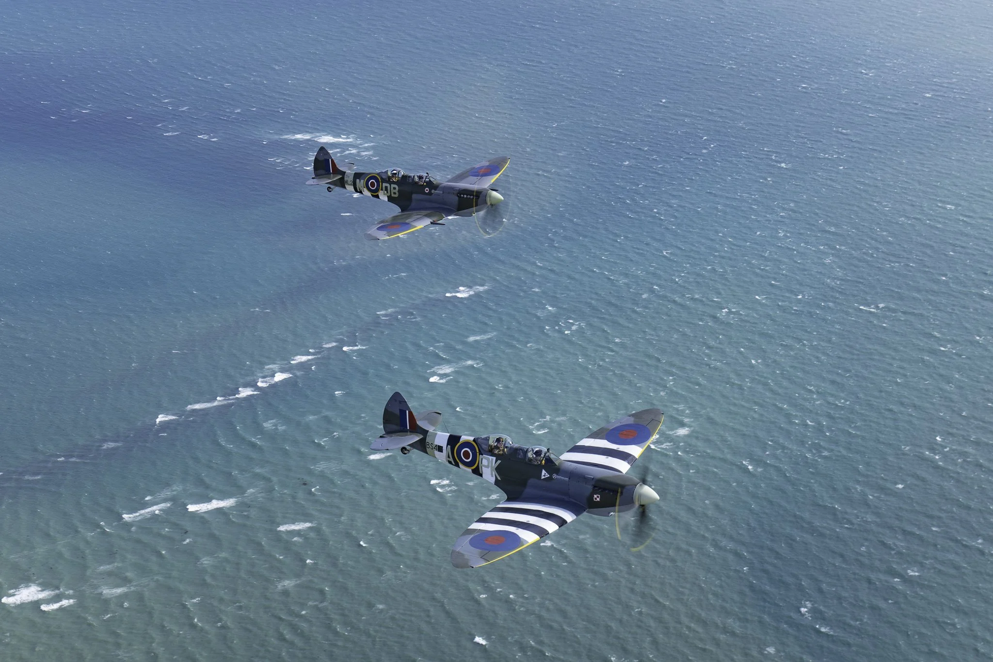 Two vintage World War II fighter planes flying in formation over the ocean.