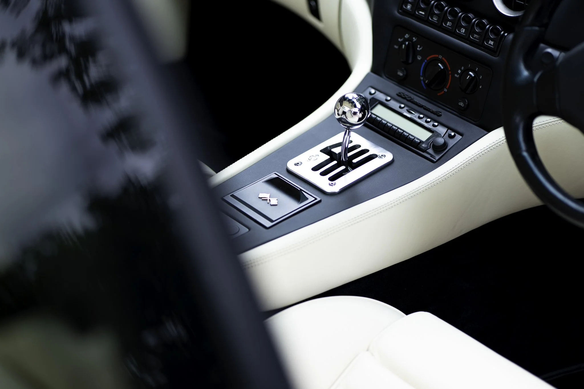 Close-up of a silver gear shifter in a car's center console surrounded by black and white interior elements, including climate control knobs and a radio.
