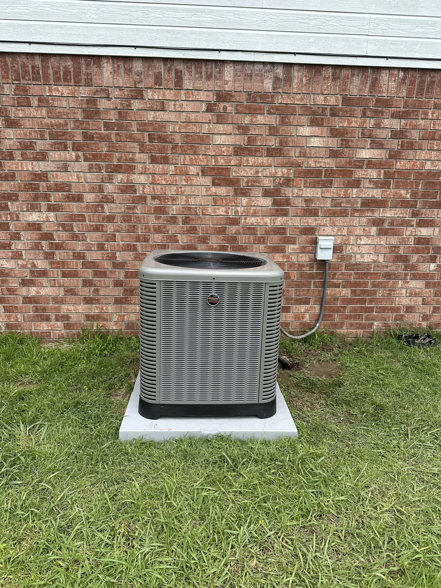 New central air conditioner condenser installed by Clark HVAC beside a brick home