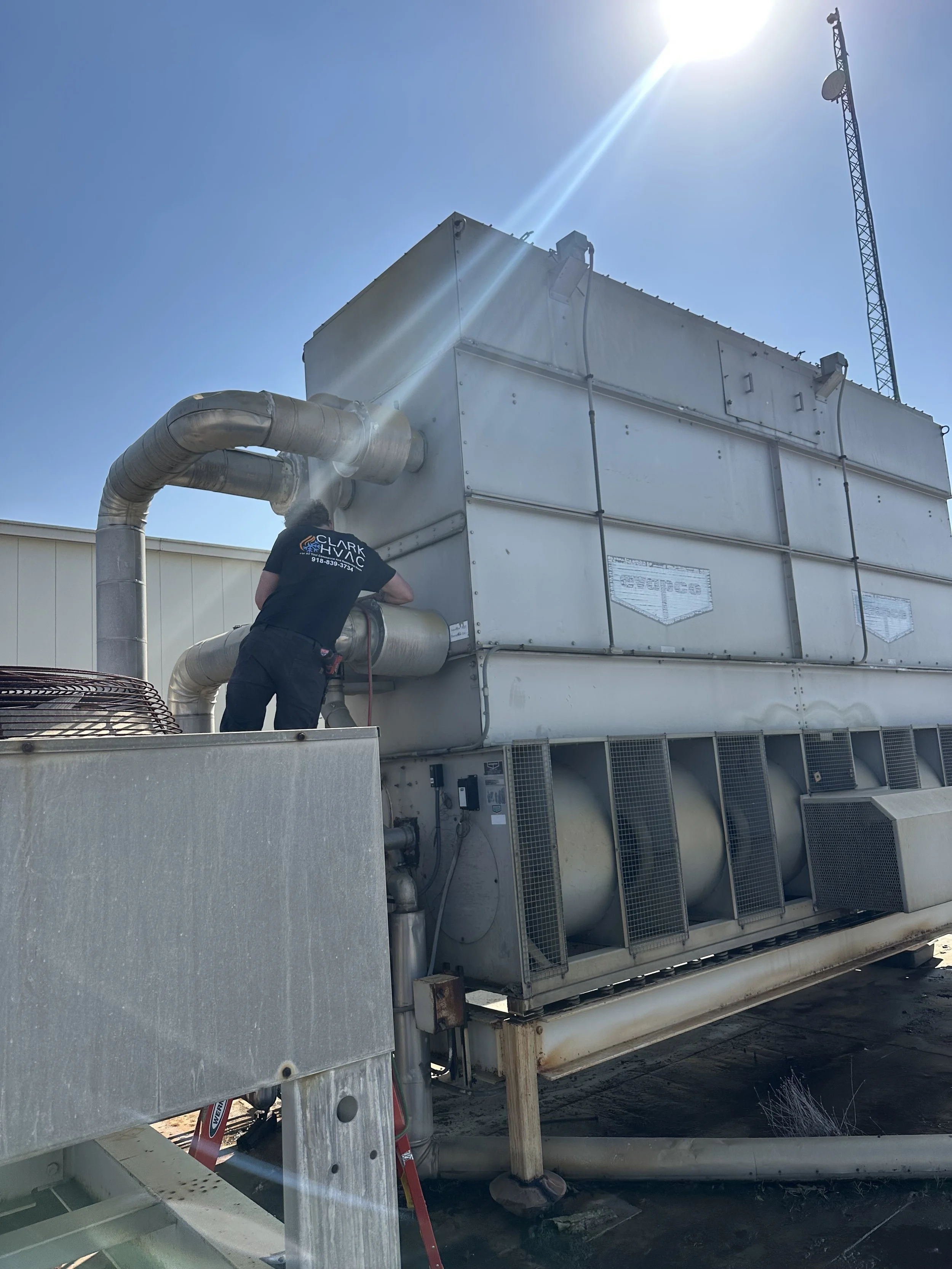 Clark HVAC technician servicing a commercial Evapco cooling tower on a Fort Smith area rooftop