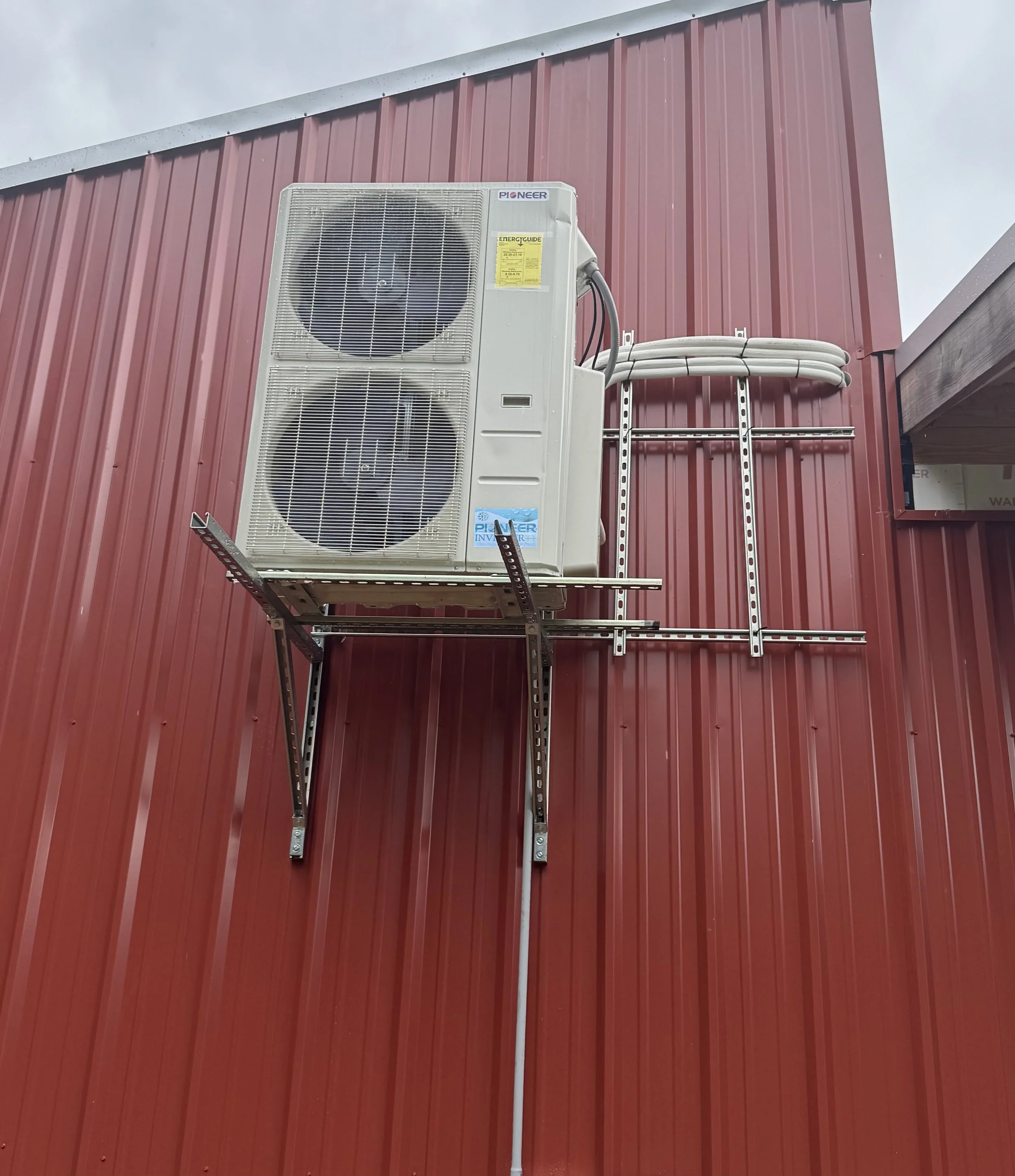 A newly installed ductless mini-split outdoor condenser unit mounted on a metal shop building. Clark HVAC specializes in energy-efficient mini-split installations for garages, barndominiums, and home additions in Poteau, Pocola, and Spiro, OK.
