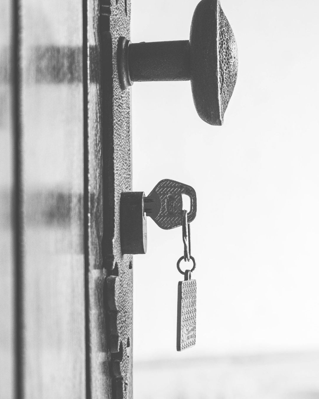 A close-up black and white photo of a door lock and key, with the key in the locked position, attached to the lock.