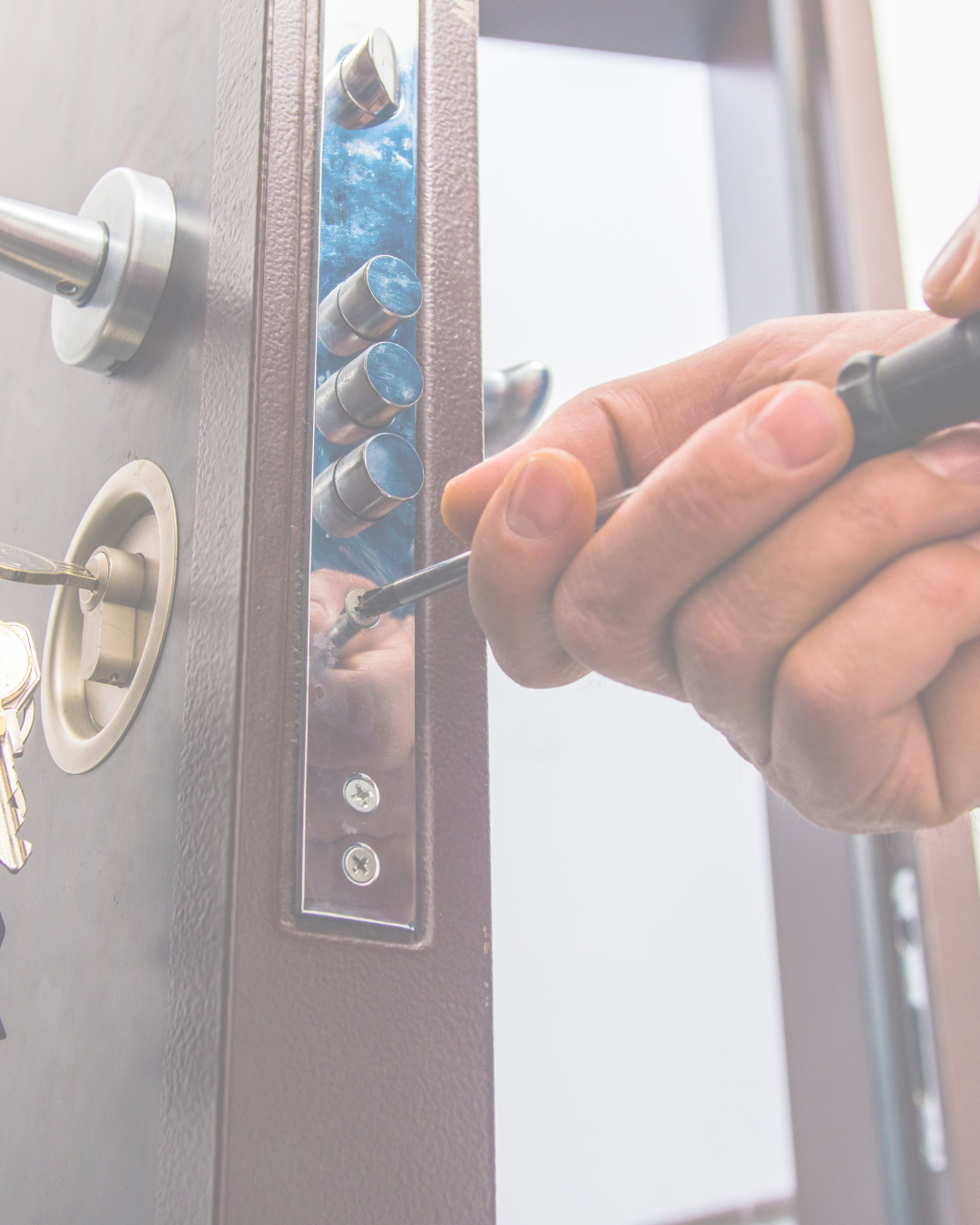 A person using a screwdriver to work on a keypad lock, with keys hanging nearby.