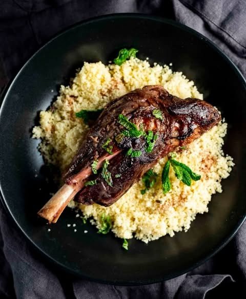 Cooked beef short rib served over a bed of couscous with chopped parsley on top, in a black bowl.