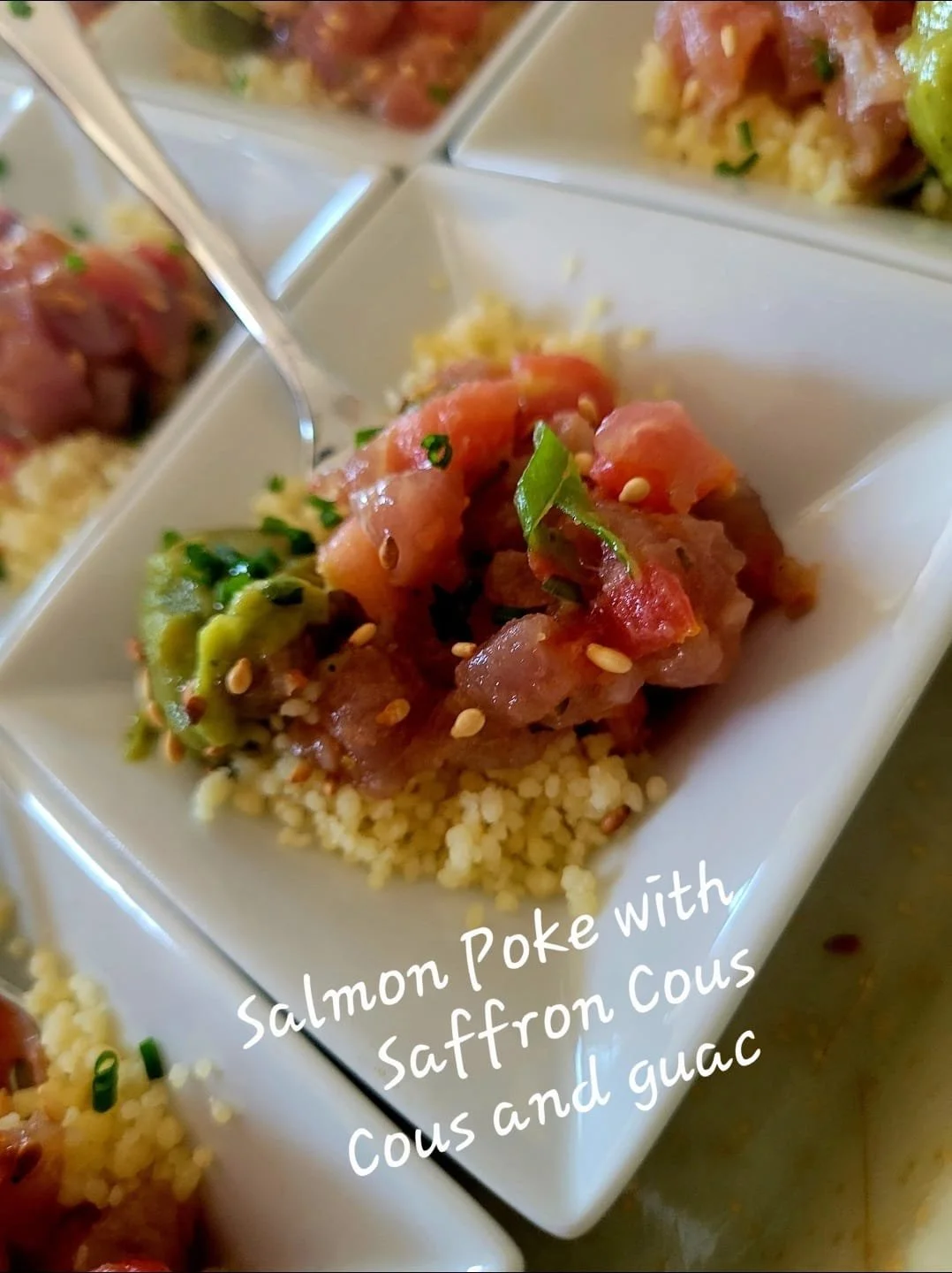 A plated serving of salmon poke with saffron couscous and guacamole, garnished with sesame seeds and chopped green onions.