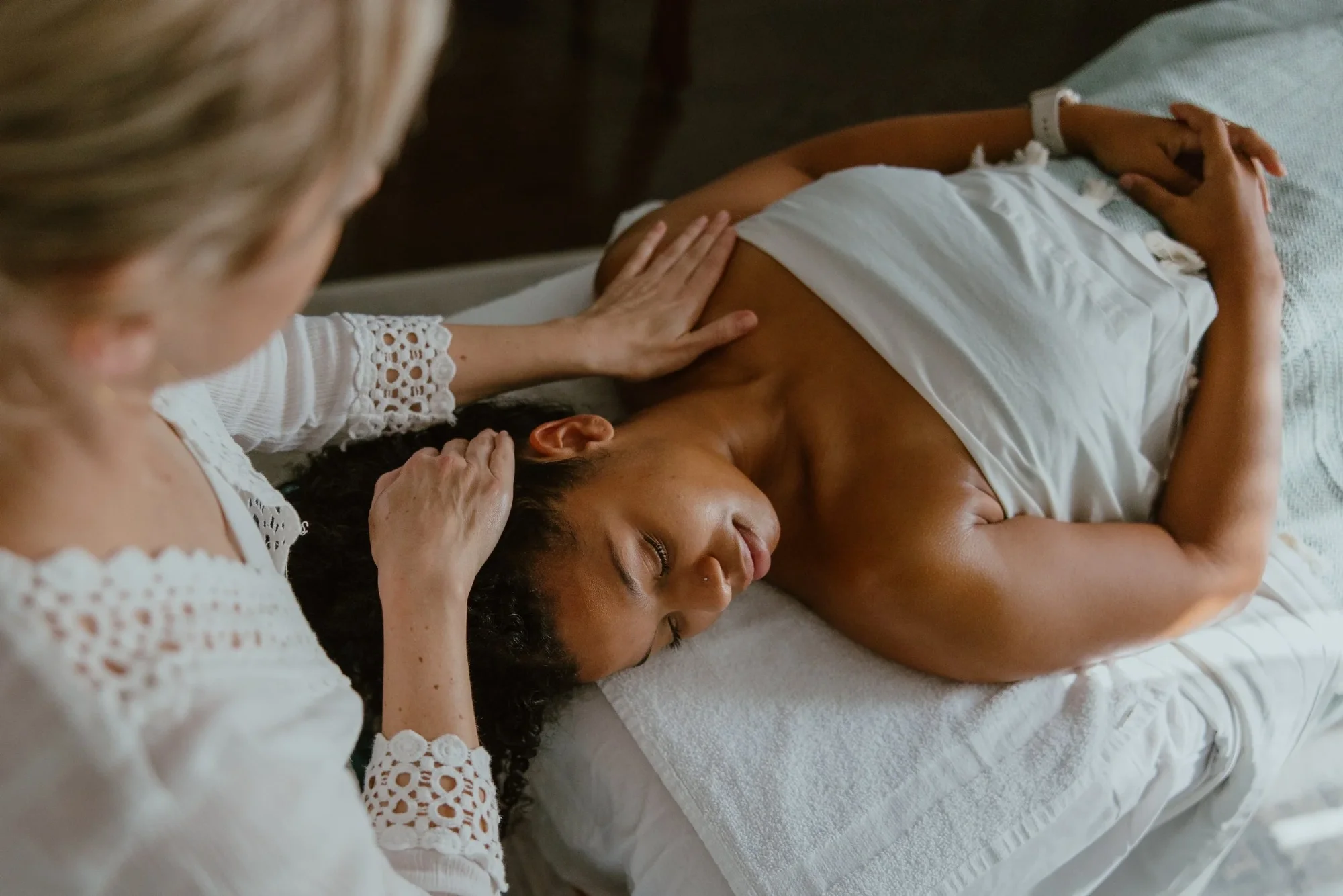 A woman receiving a facial massage from Suzy at Urban Holistic in Hamilton on a white massage bed.