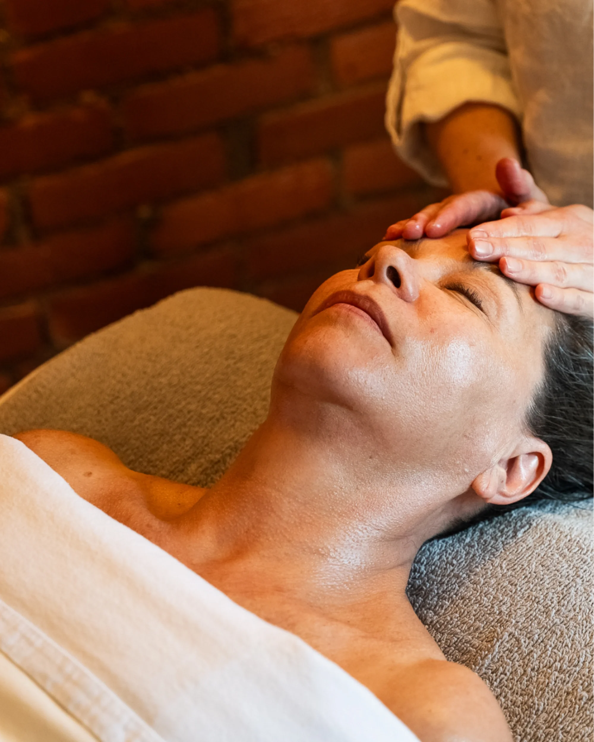 A woman laying face-up, receiving a facial massage from Suzy at Urban Holistic in Hamilton