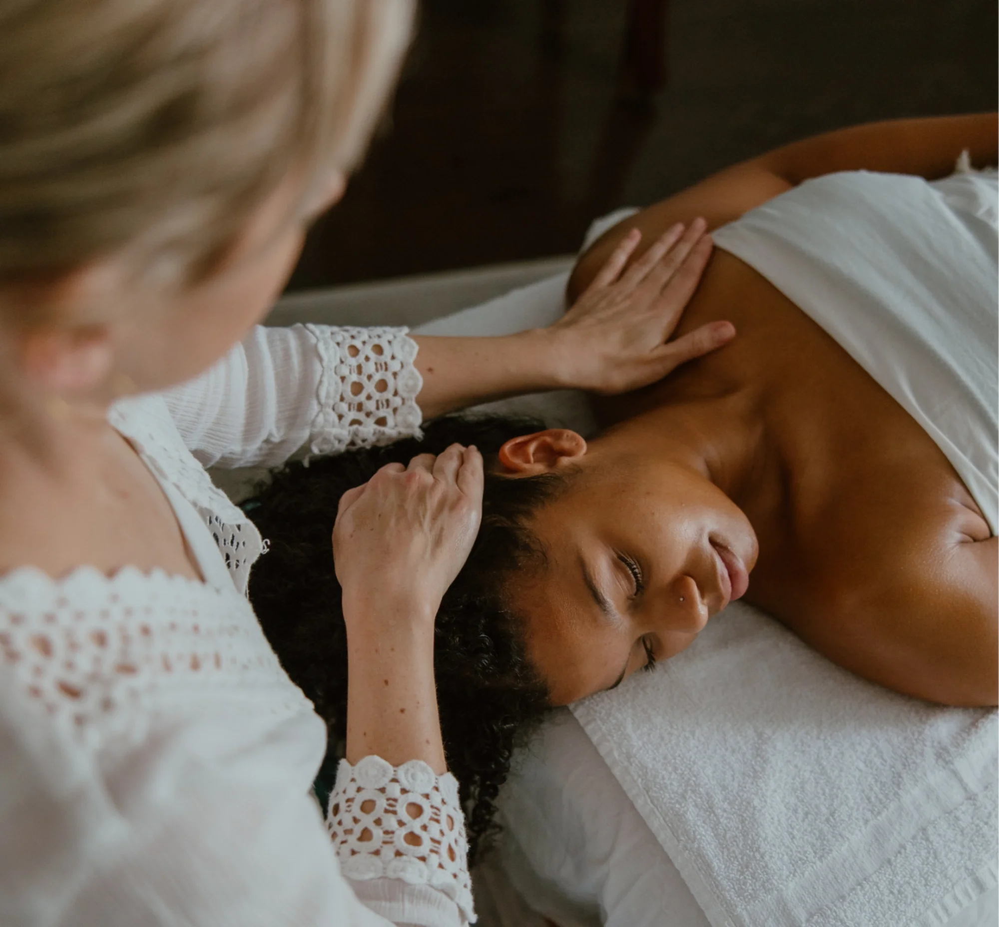 A woman receiving a facial massage from Suzy at Urban Holistic in Hamilton on a white massage bed.
