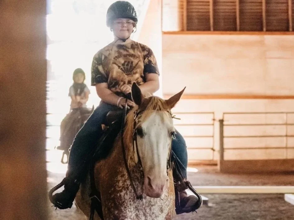Two smiling girls with glasses and a woman petting a horse with a blond mane outdoors.