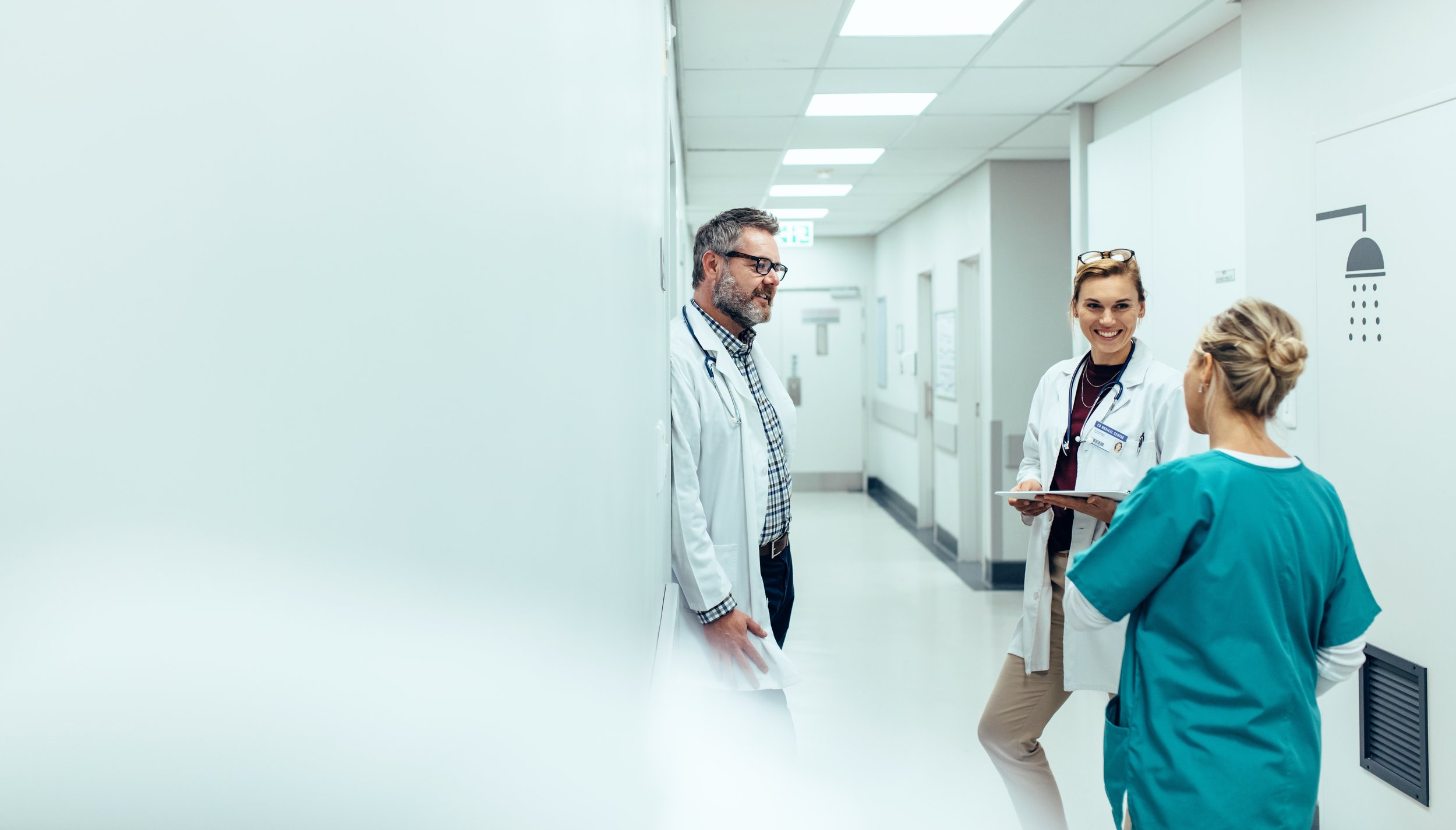 Three healthcare professionals, including one man and two women, are standing in a hospital hallway, engaged in conversation.