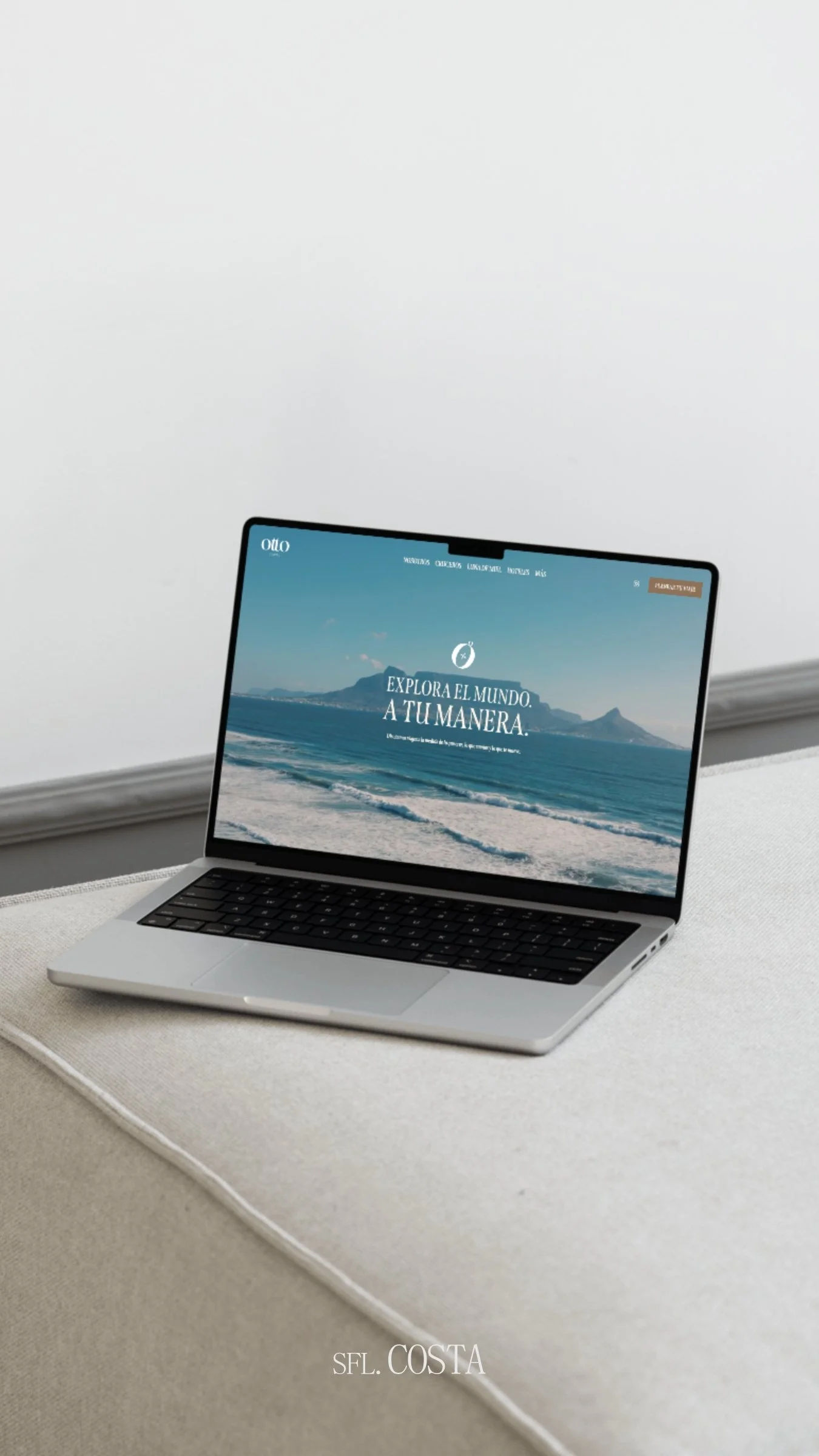 A laptop on a desk showing a website with beach and mountain scenery, and Spanish text 'Explora el mundo a tu manera'.