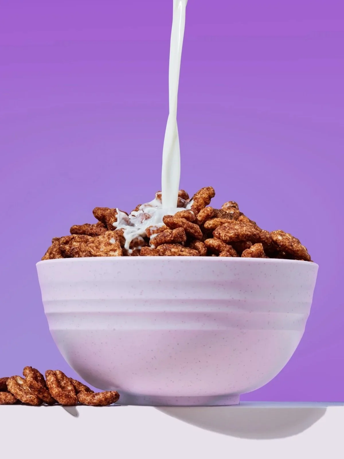 A pink bowl filled with crispy fried chicken pieces, with milk being poured over it, against a purple background.