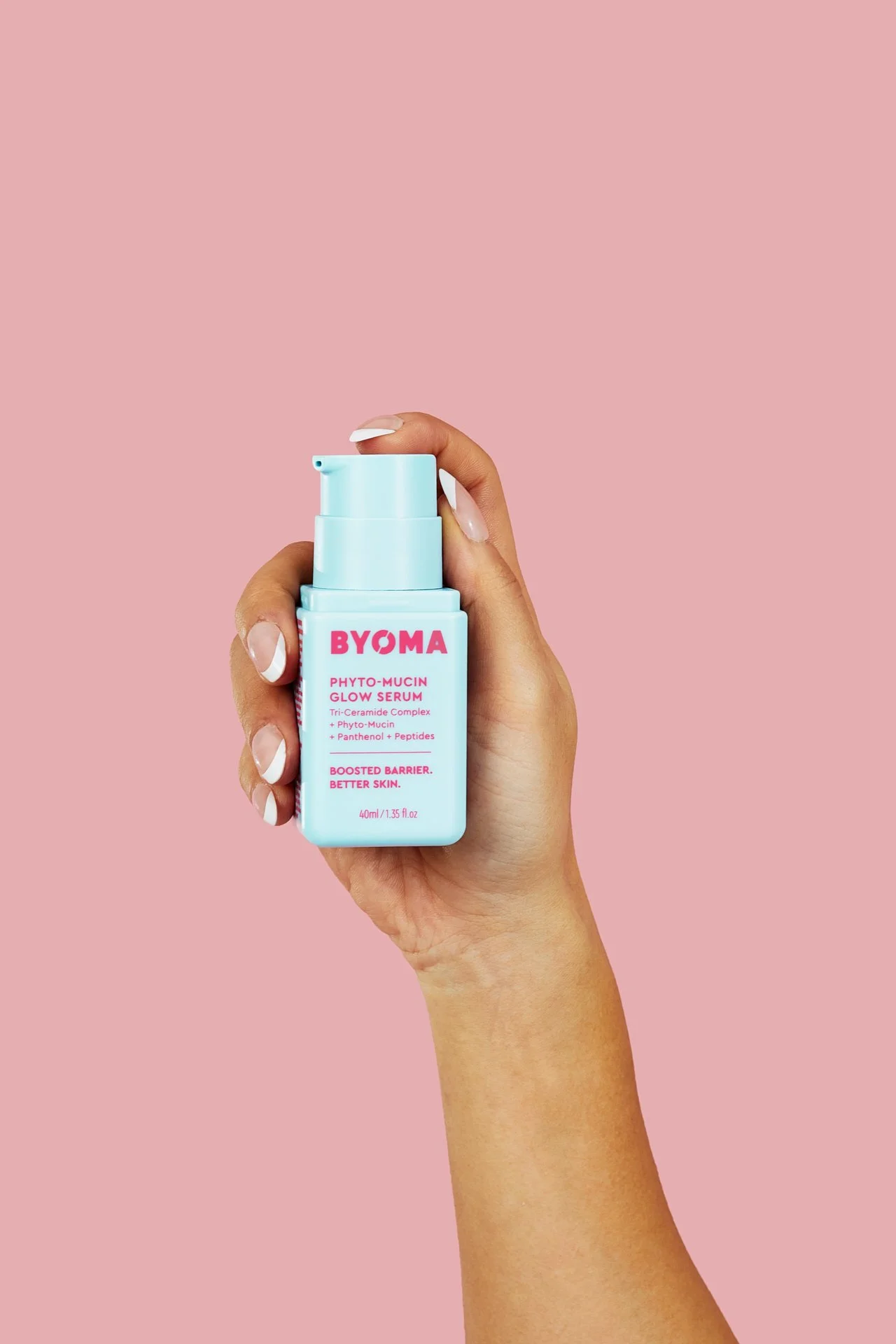 A hand holding a blue bottle of BYOMA Phyto-Mucin Glow Serum against a pink background.