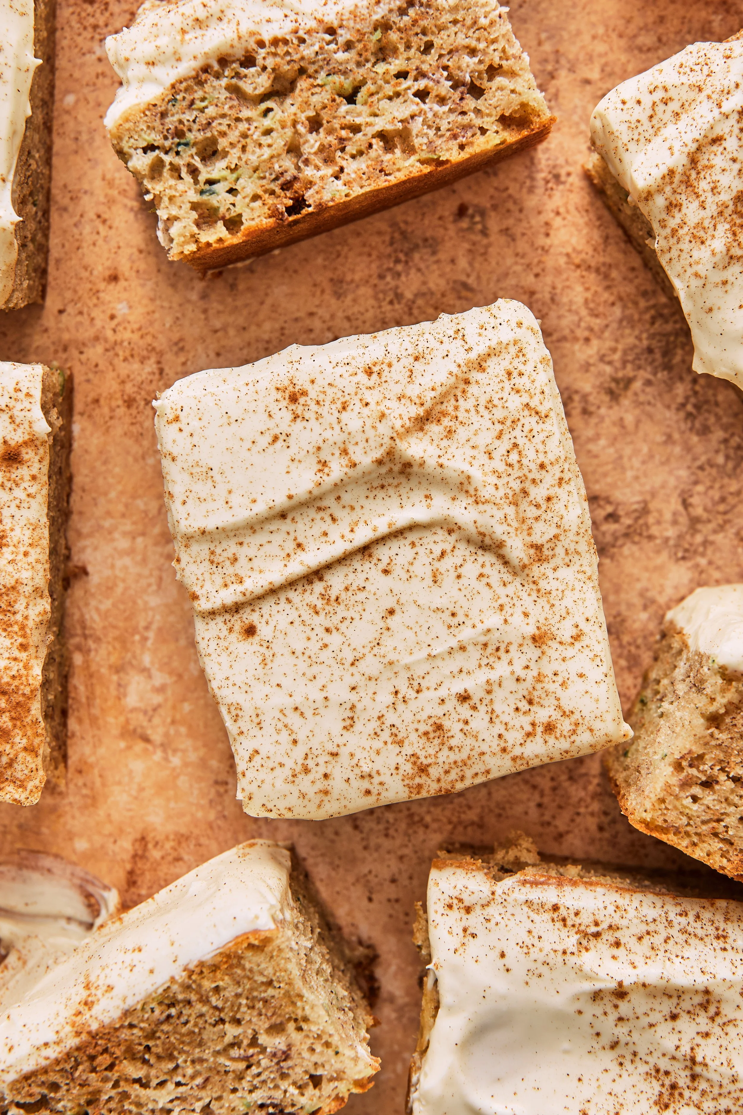 Slices of cake with cinnamon and cream cheese frosting on parchment paper.