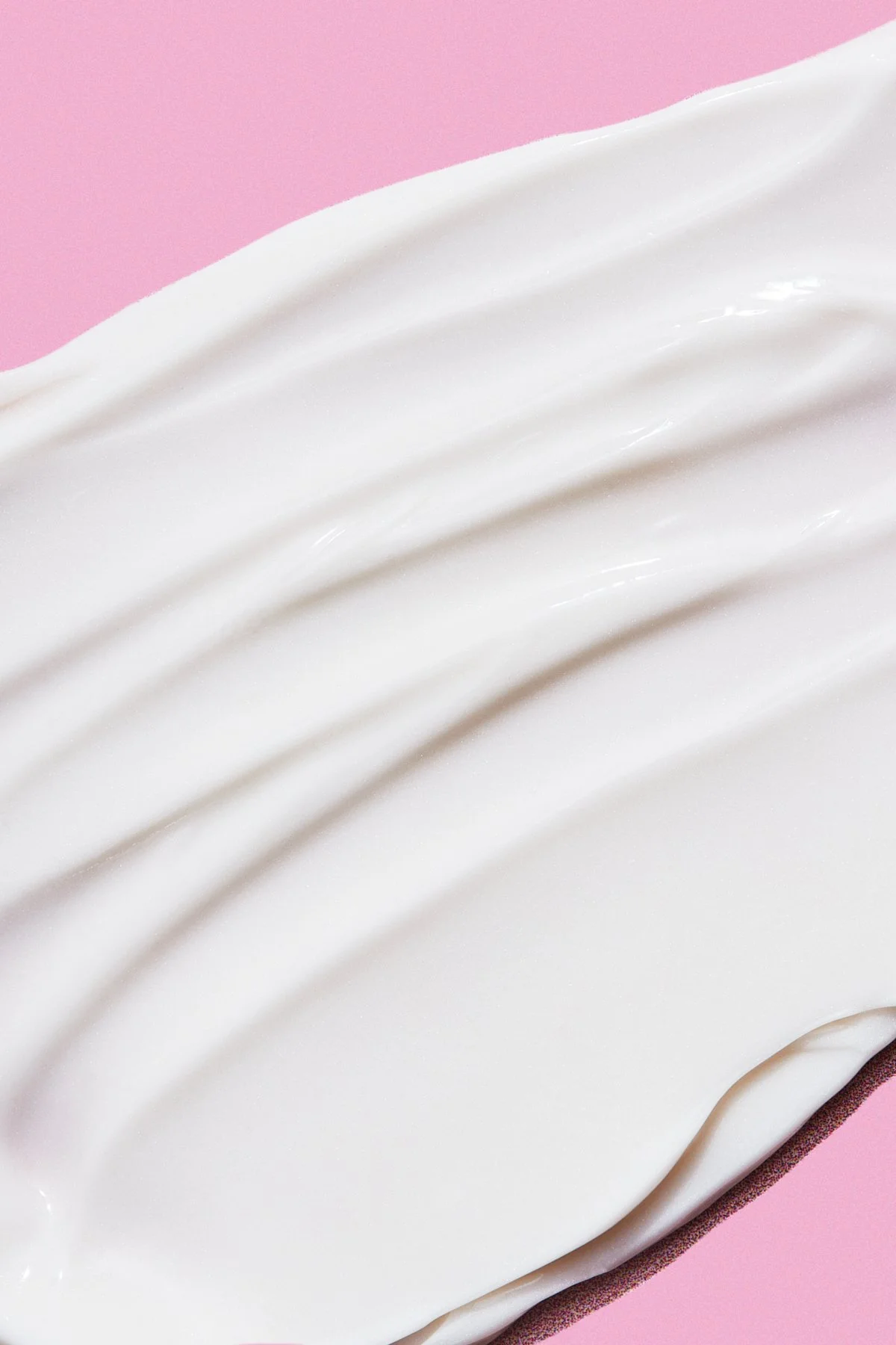 Close-up of white cream or lotion spread on pink surface.
